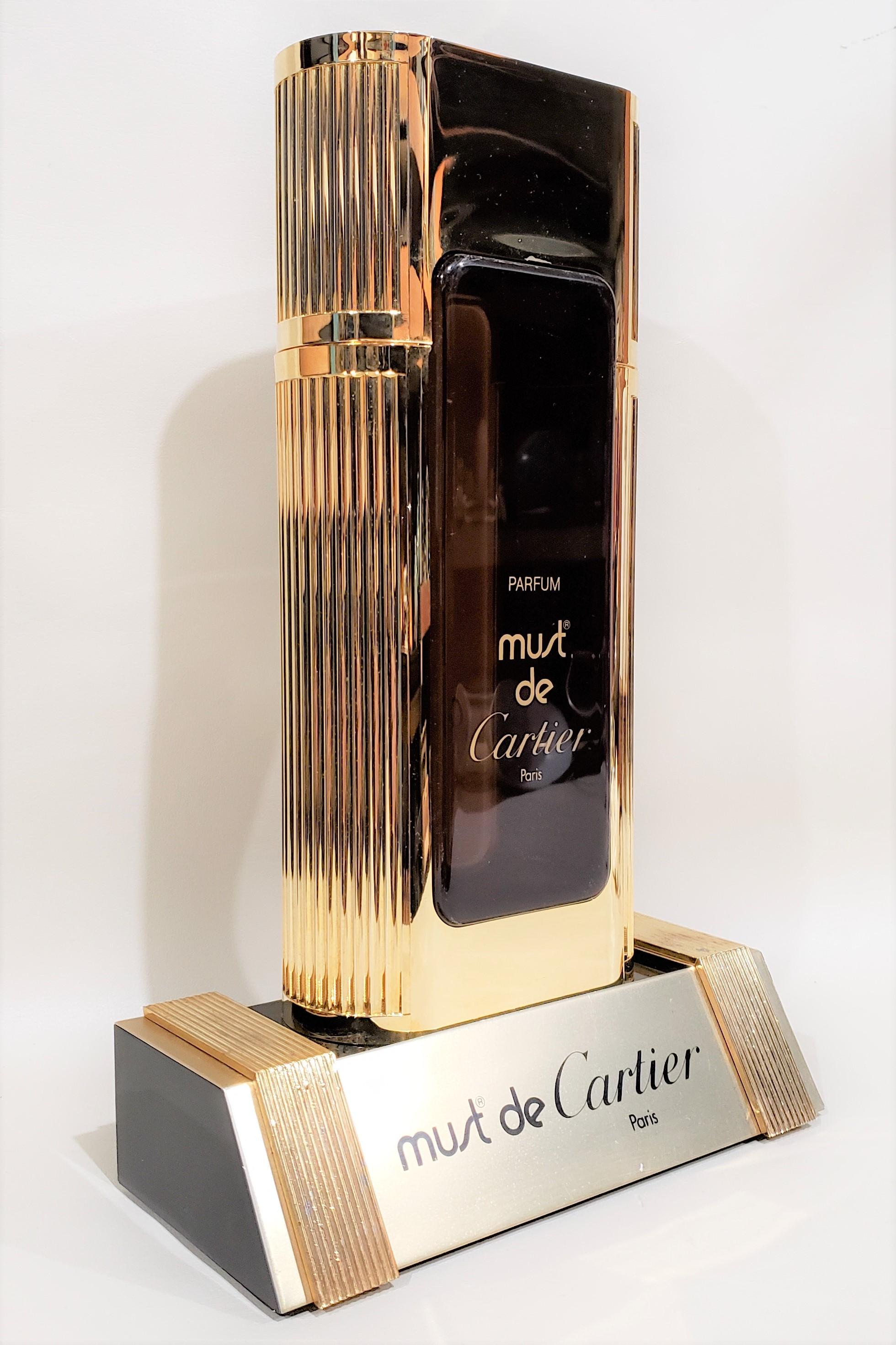 Flacon de parfum factice Must de Cartier présenté en magasin avec un support. Ne contient pas de parfum et est utilisé pour l'affichage uniquement.