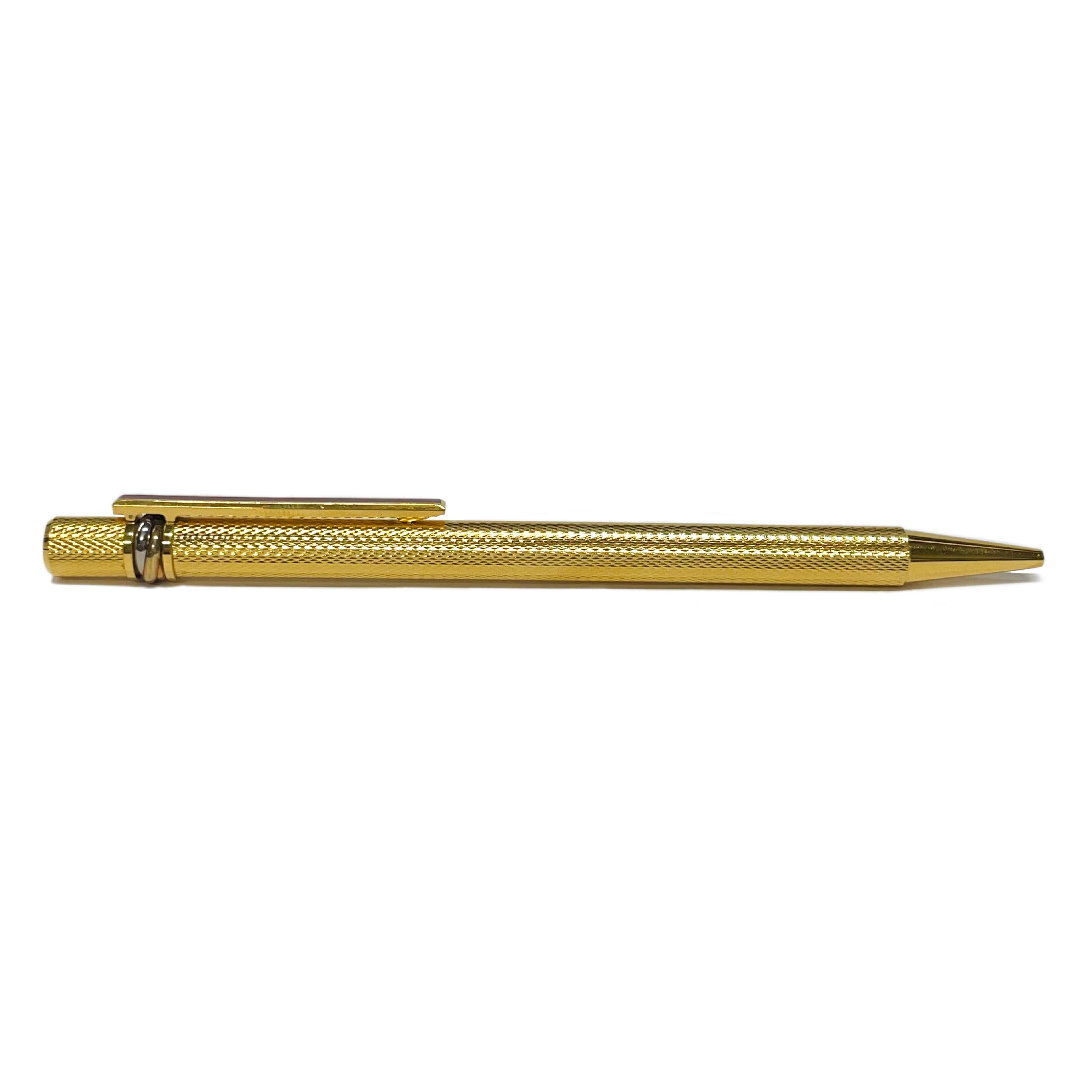 From the house of Cartier comes this lovely writing instrument, the Must de Cartier Gold Plated Ballpoint Pen. A simply elegant design with a trinity band, textured gold-plated barrel, and a smooth clip with a Cartier red enamel inlay. This piece