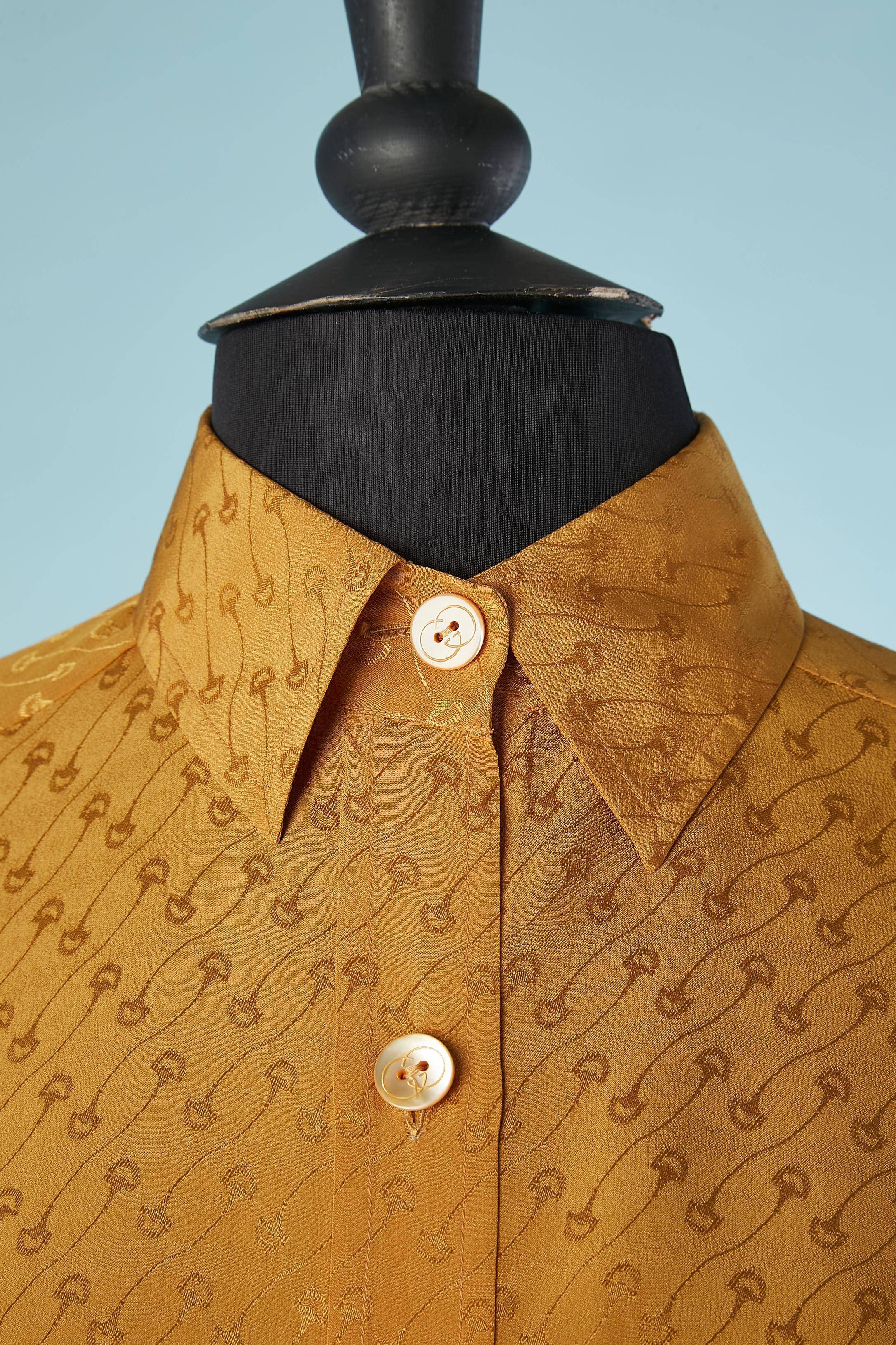 Mustard silk jacquard shirt. Branded buttons. 
Shoulder pads. Box pleat on the side in the front and back.

Guccio Giovanbattista Giacinto Dario Maria Gucci (26 March 1881 – 2 January 1953) was an Italian businessman and fashion designer. He is