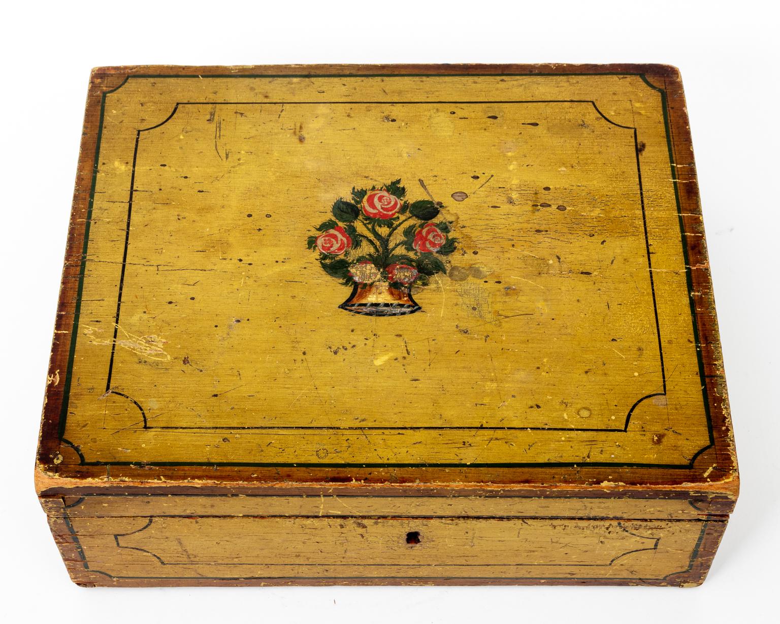 Circa 1825 pinewood American trinket box in original mustard yellow paint with painted linear trim on the exterior and a floral medallion on the lid. The piece also features foil lining on the interior. Made in the United States. Please note of wear