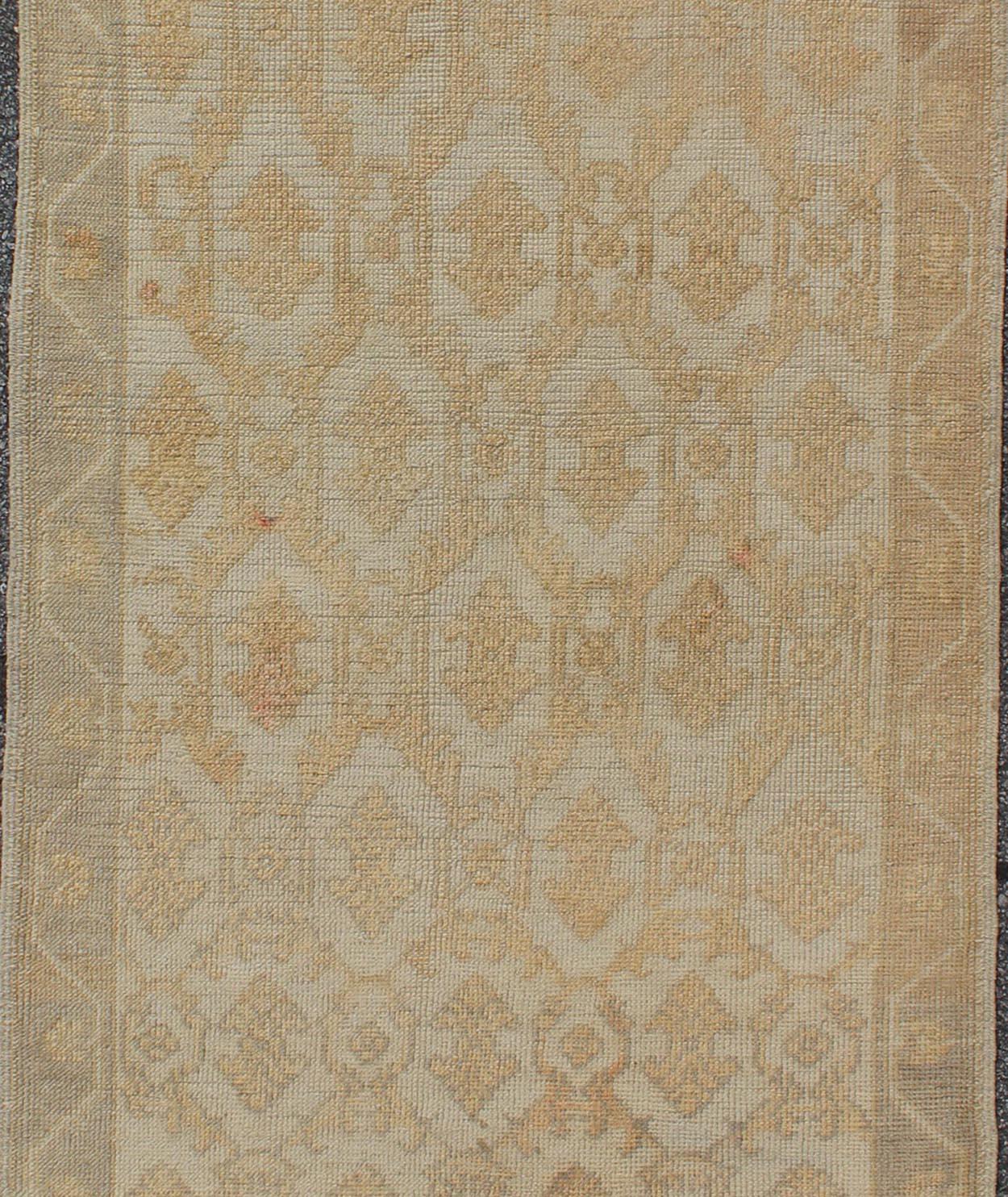Measures: 3'3 x 8'7

Set on a cream-colored field with an all-over similarly-toned pattern, this beautiful midcentury Turkish Oushak rug (circa 1950) features cross-latch and lattice work framing double arrow-heads. A simple vining border frames the