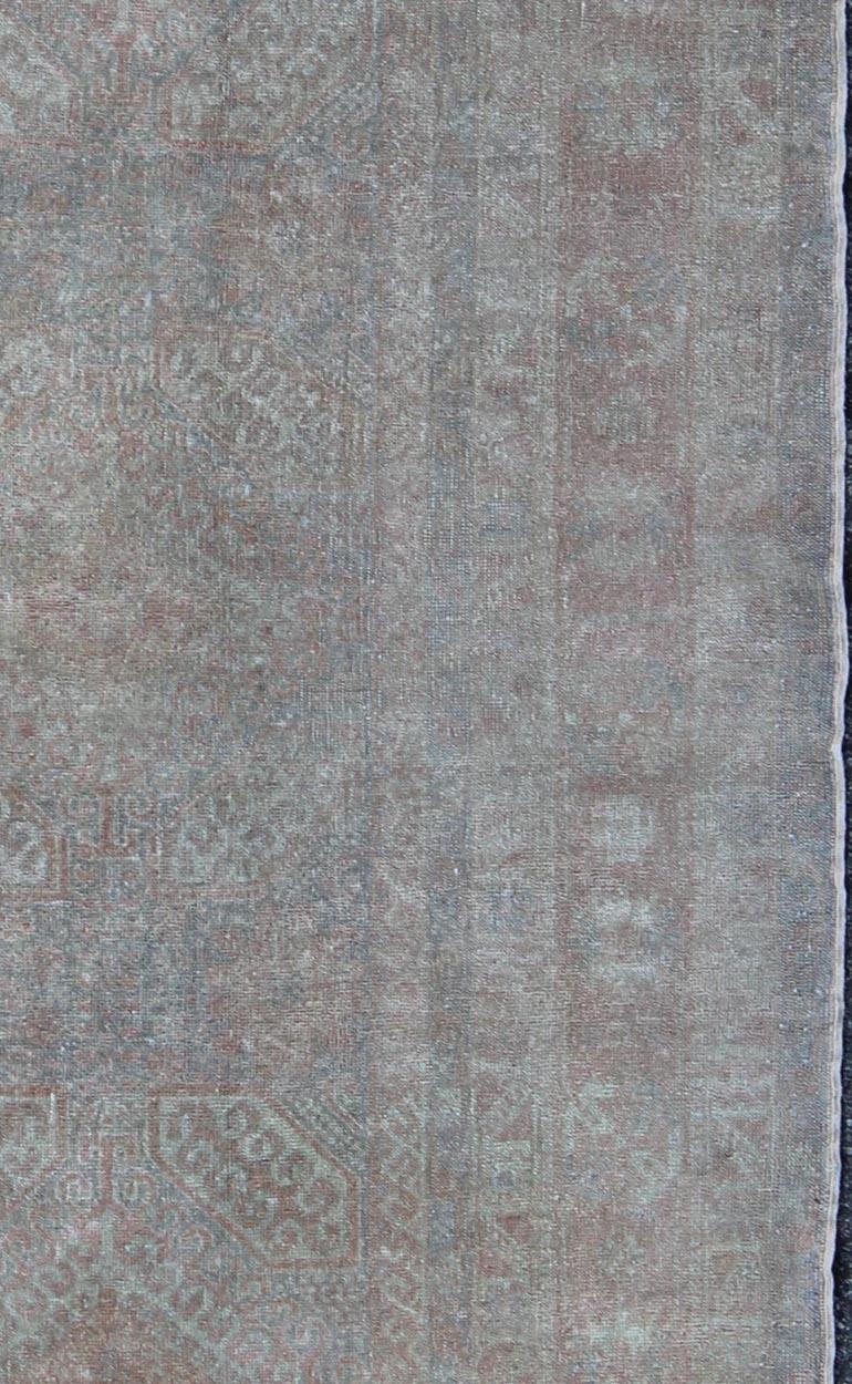 This antique Turkish Oushak rug features a muted design and soft colors of light green, cream and salmon. The large, multi-banded border frames the designs floating in the central field, and the entirety of the rug is rendered in various subdued