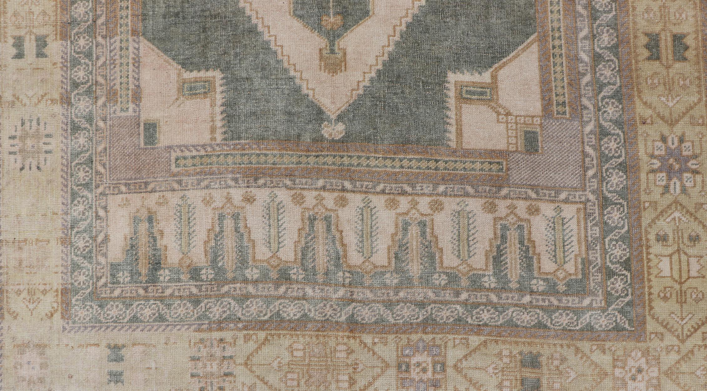 This vintage muted Turkish Oushak Rug has been hand-knotted in wool and features a sub-geometric medallion design rendered in cream, green, ivory and marigold tones. A complementary, multi-tiered border encompasses the entirety of the piece; making