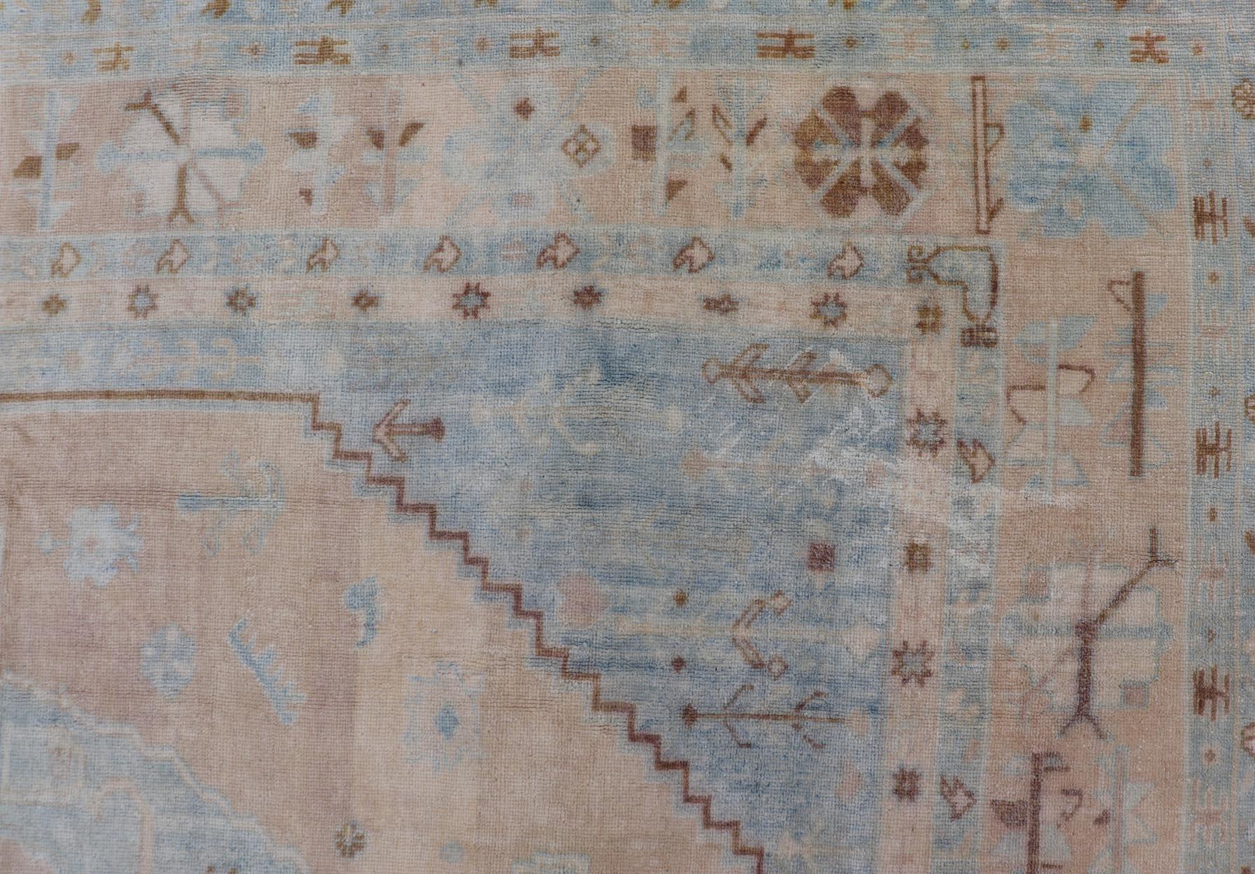 Ce tapis turc Oushak vintage a été noué à la main en laine et présente un motif subgéométrique dans des tons sourds de beige et de bleu. Une bordure complémentaire à plusieurs niveaux englobe la totalité de la pièce, ce qui lui permet de s'adapter