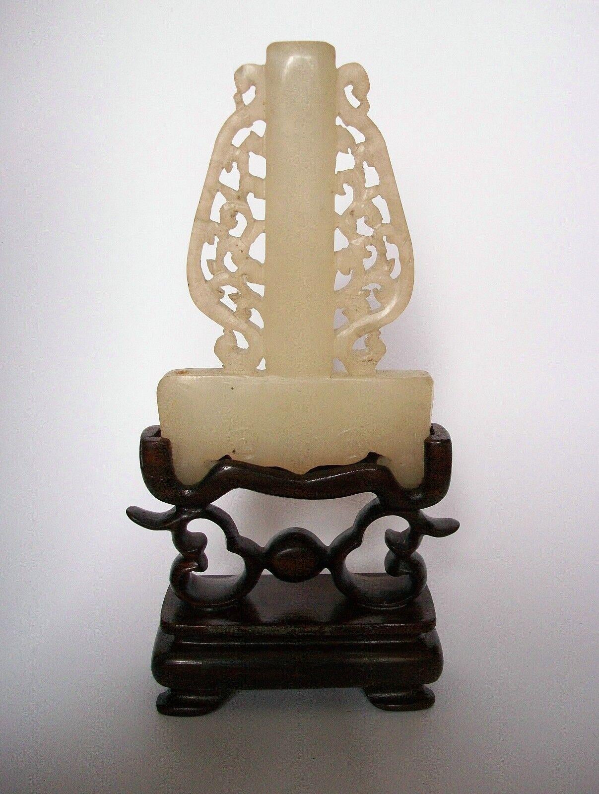 Mutton Fat jade amulet carving on elaborate hardwood stand - the hand carved jade with pierced scrolling vines and solid base and central column - the hand carved fitted stand featuring clouds above a plinth and raised on four scrolling feet -