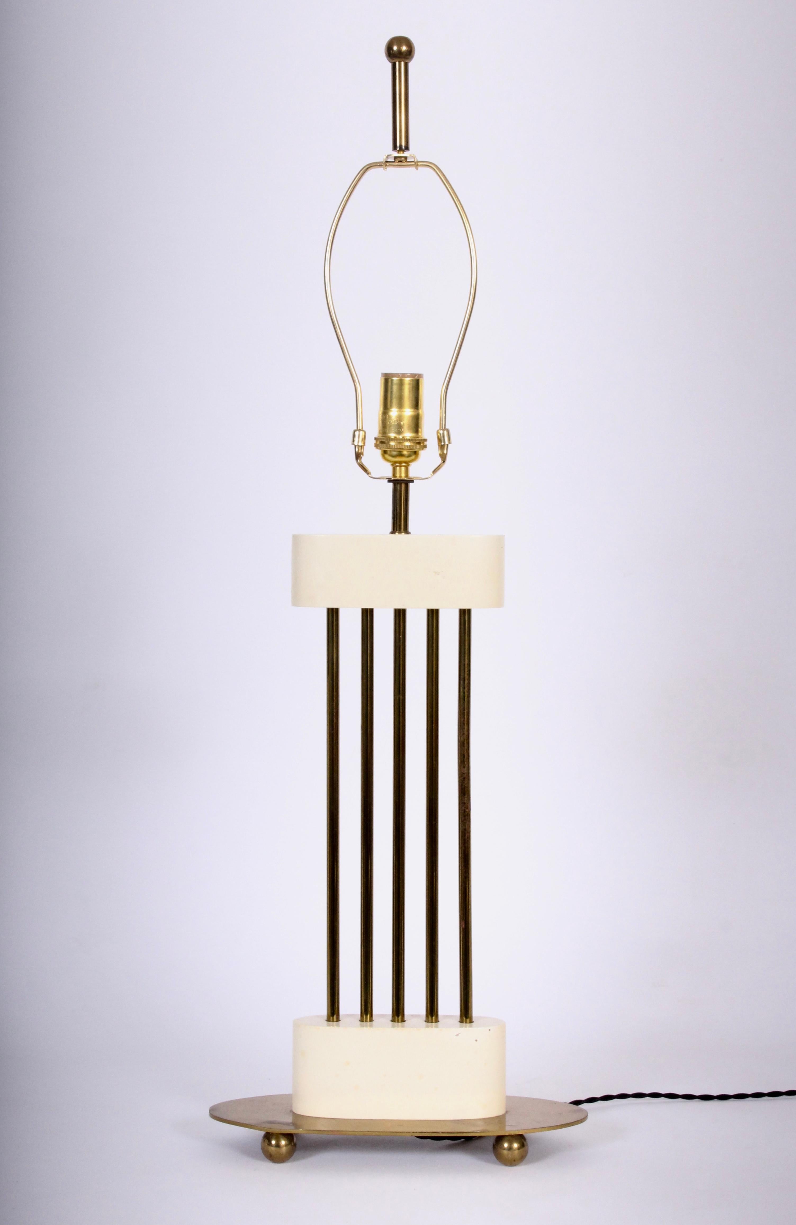 Tall Hollywood Regency Mutual Sunset Lamp Co. warm white enamel and brass table lamp, in the style of Tommi Parzinger. Featuring an open oval framework with five Brass rods encased in white cream enameled wood on oval brass atop a footed ball base.