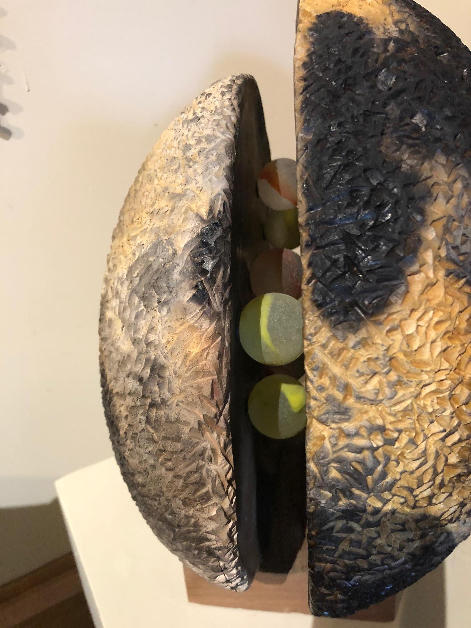 An abstract round sculpture suggesting a planet, having two halves of gorgeously fired and carved clay with glass round marbles inside. By renowned artist Connie McIndoe.