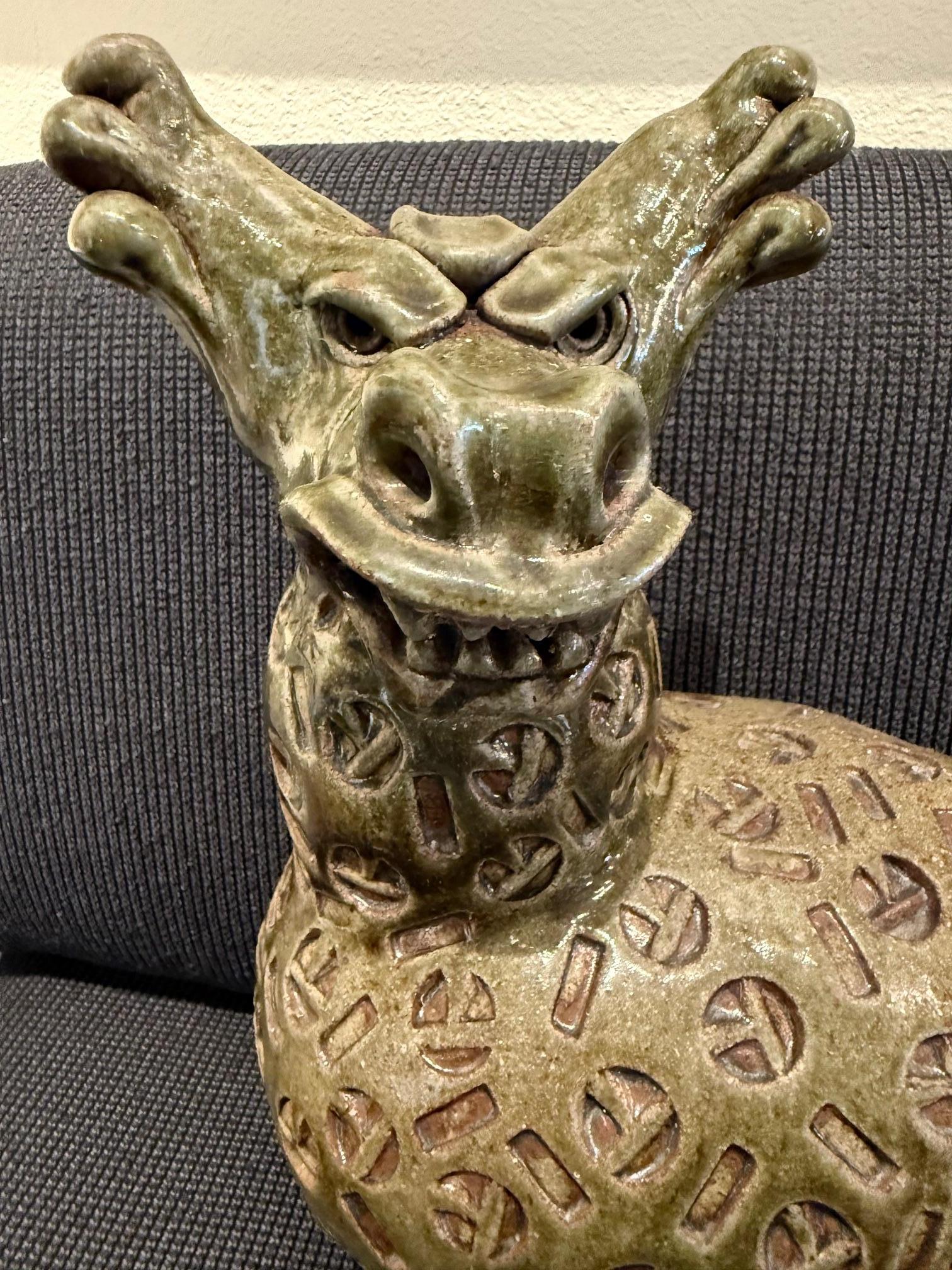Cette sculpture en céramique de Dora De Larios, à la fois fantaisiste et imposante, représente une bête fantastique, dont le rictus et la tête à deux cornes lui confèrent à la fois humour et menace. Son corps rond, orné de motifs circulaires