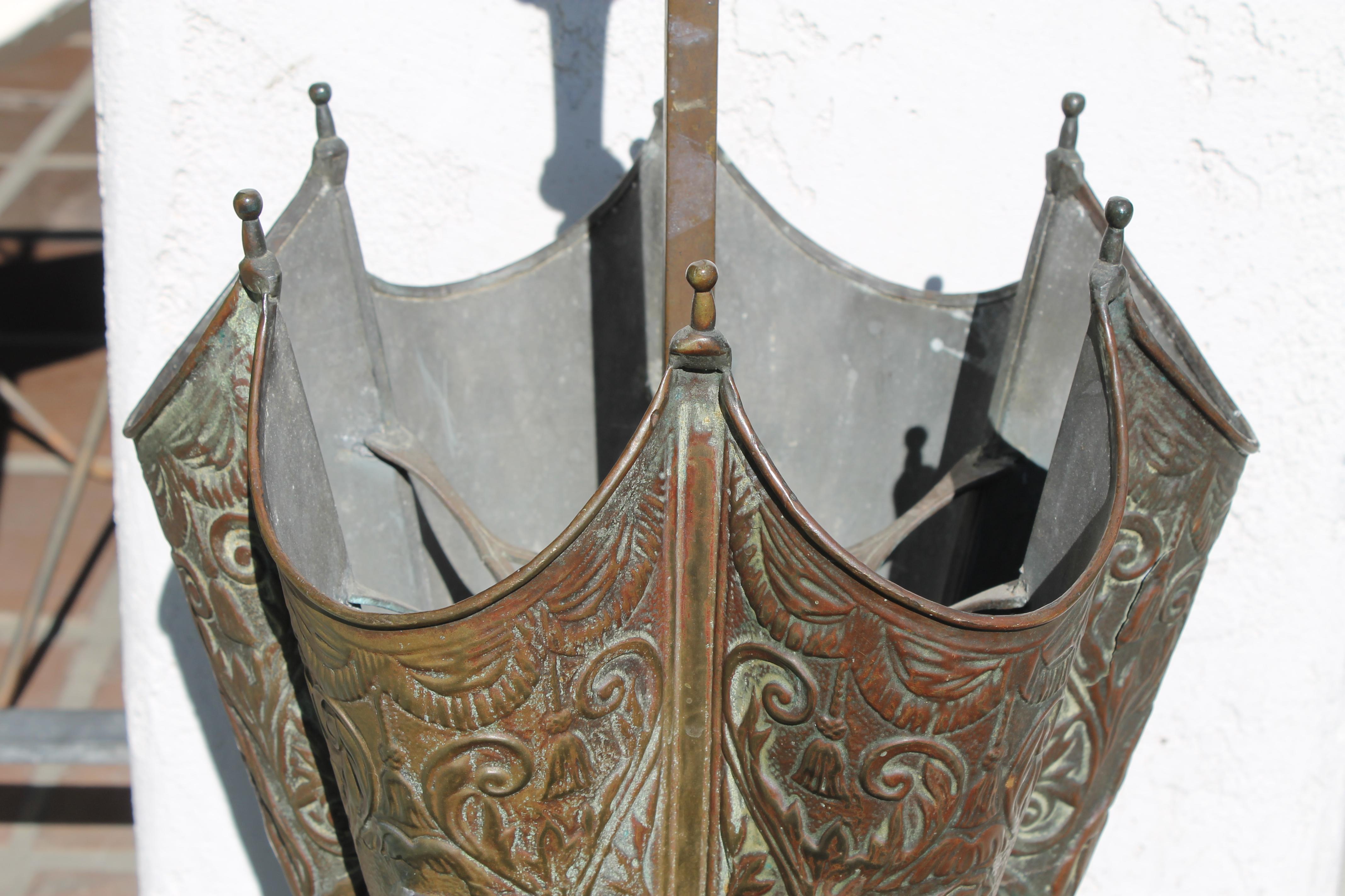 Schirmständer aus Kupfer mit stilisierten Figuren mythologischer Wassergötter. Der Schirmständer hat einen Durchmesser von 13