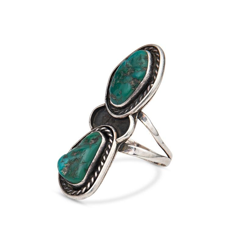 This vintage sterling silver ring features two natural turquoise stones set vertically accented by braiding details set on a double shank. The ring measures approximately 1.75