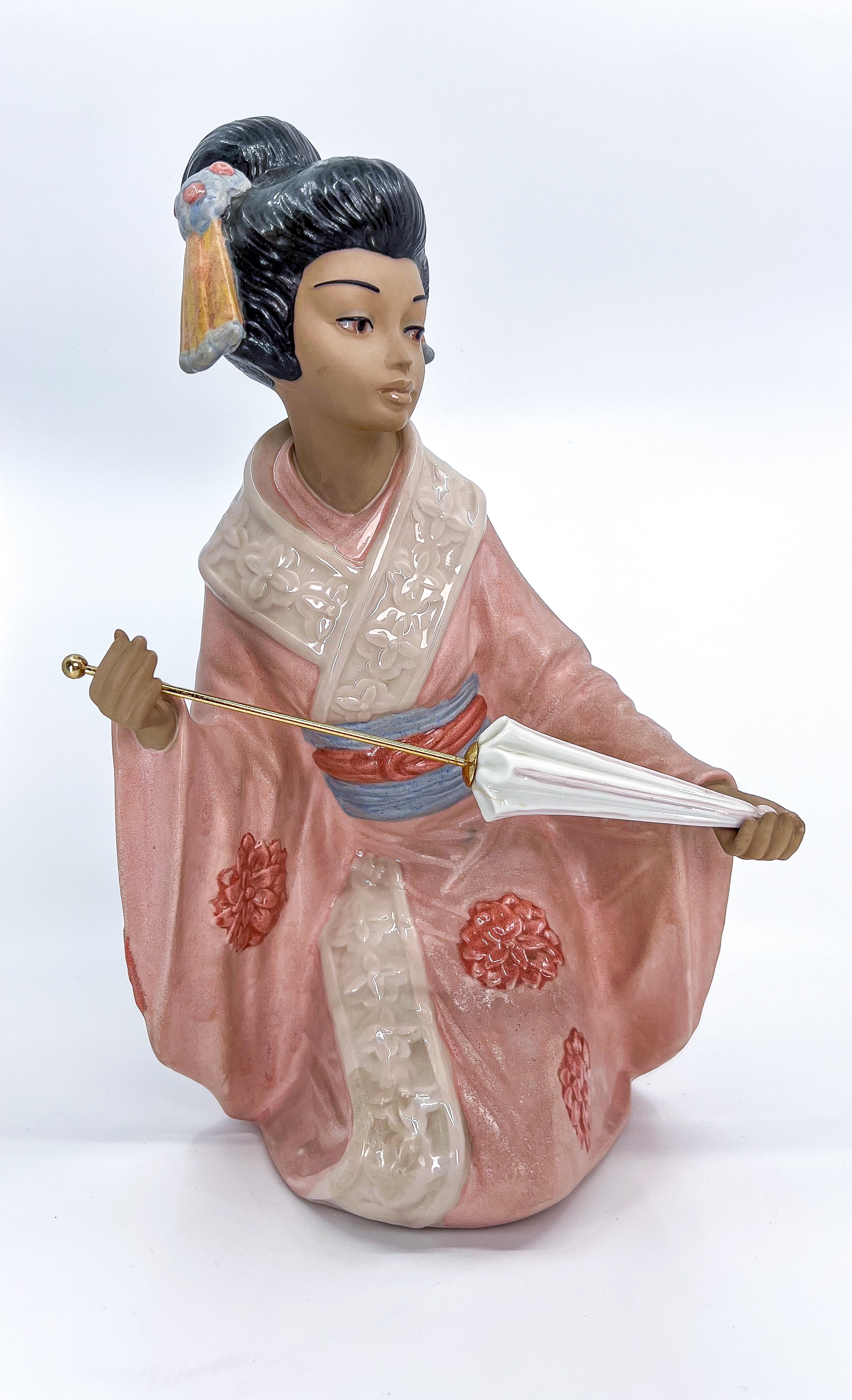 Nadal porcelain figurine Geisha in pink dress with flowers and parasol.

The Japanese Geisha has spent much time and careful attention in order to look beautiful. She is dressed in all her magnificent finery. Her kimono is covered with red flowers