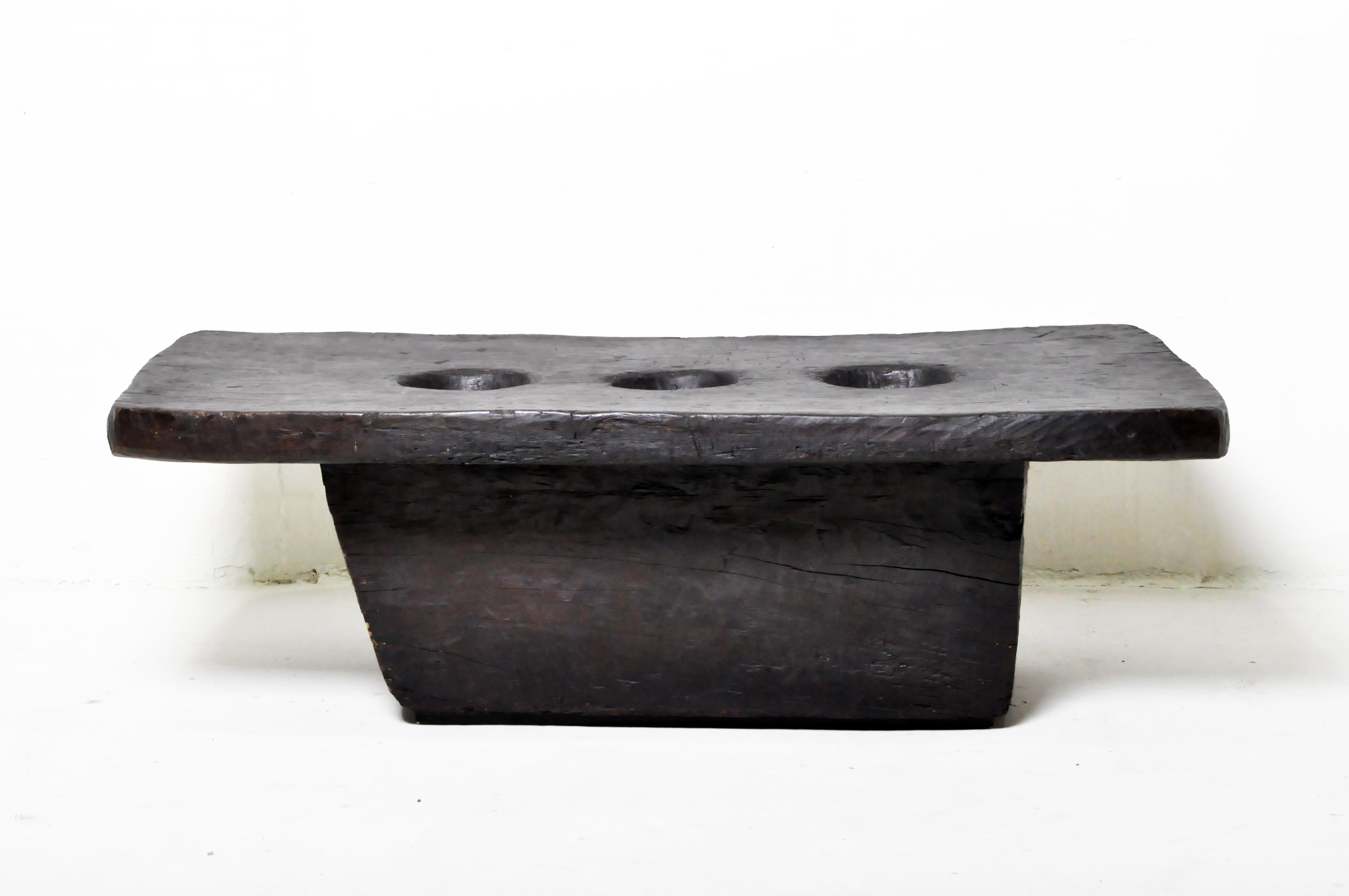 This solid wood table is actually an old rice mortar. Dry rice grain was placed in the receptacle holes and pounded by a wooden pestle. The weight of the piece kept it stable. The Naga tribe inhabits the low rainy mountains of the India-Burma border