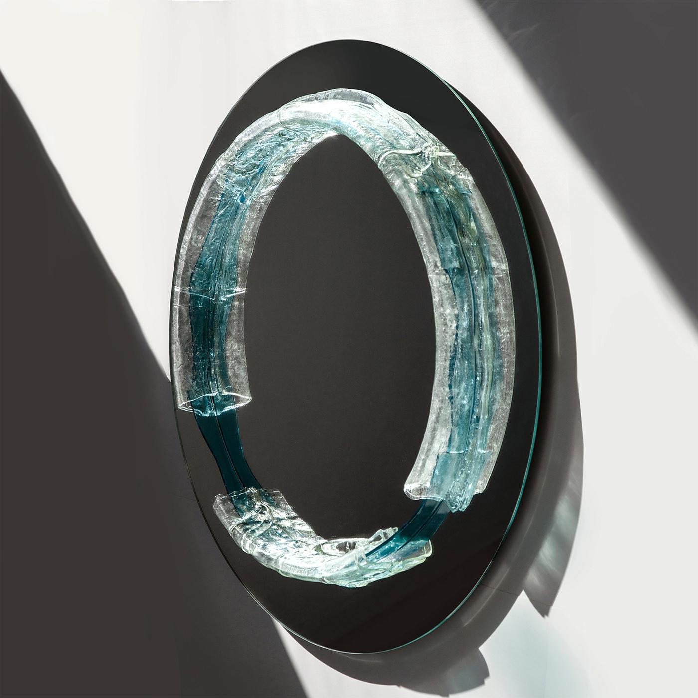 Lo specchio rotondo in cristallo Naias ha un diametro di 100 cm e presenta un elemento in vetro acquamarina fuso con cristallo riciclato. Il suo design trae ispirazione dal mito delle Naiadi, evocando il movimento e la vitalità delle sorgenti che