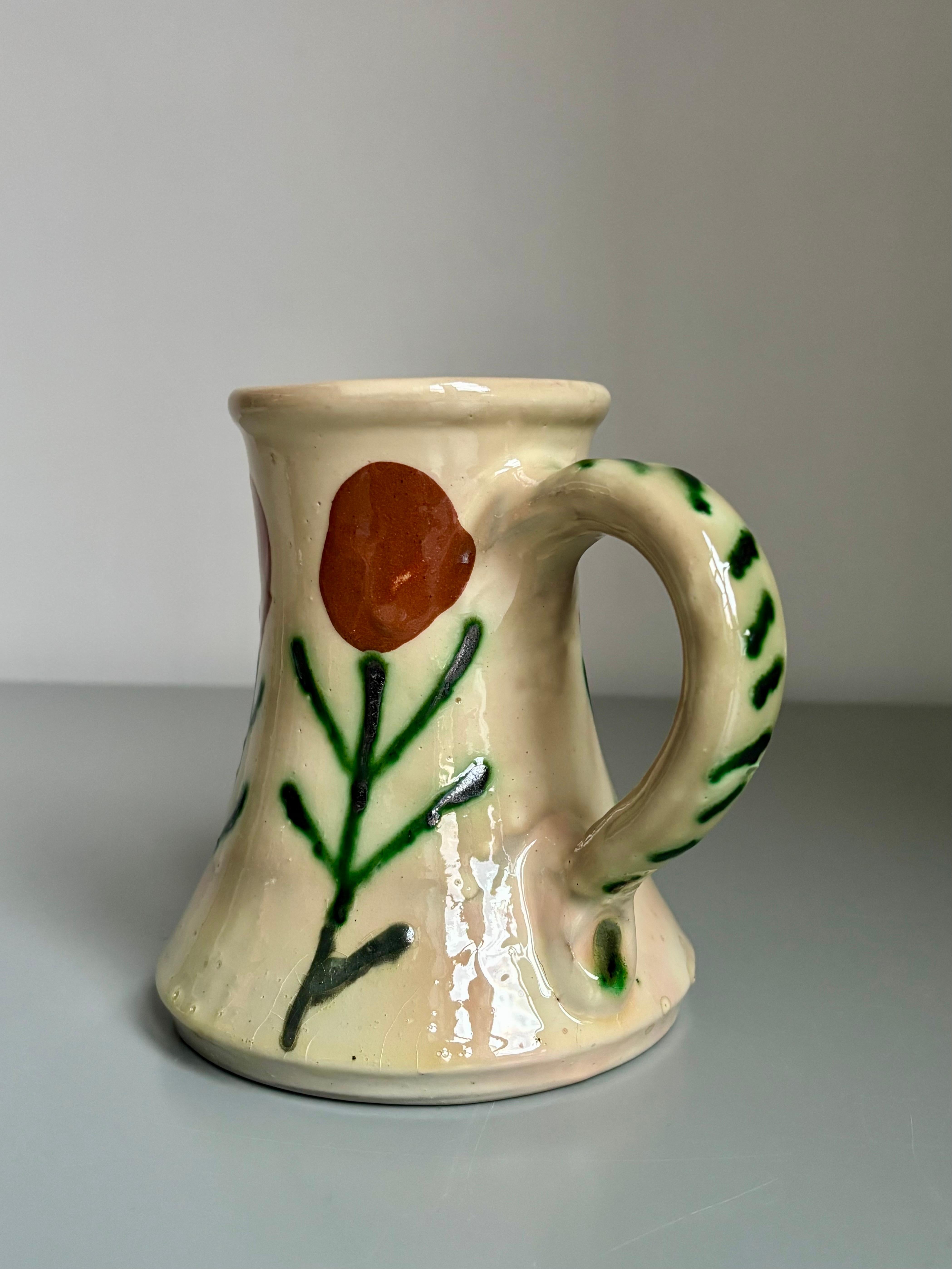 1950s handmade, hand-painted ceramic Mediterranean style pitcher vase. Simplistic red brick colored flowers on green stems on warm cream yellow base. 
Beautiful vintage condition. 
Denmark, circa 1950s.