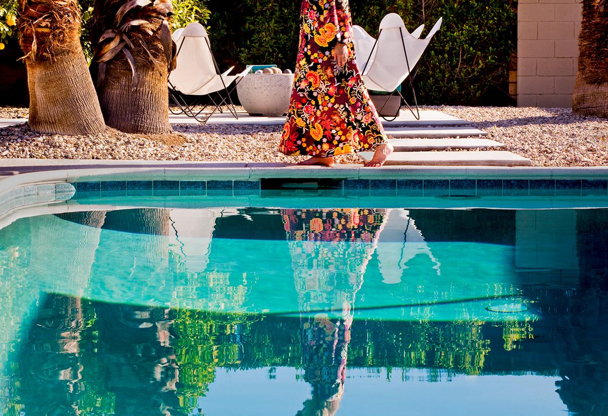 Backyard Morning by Nancy Baron is a 24 x 36 inch archival pigment print, available in an edition of 5. This photograph features a woman walking in her backyard next to a pool in Palm Springs. This photograph is from Nancy Baron's series, Palm