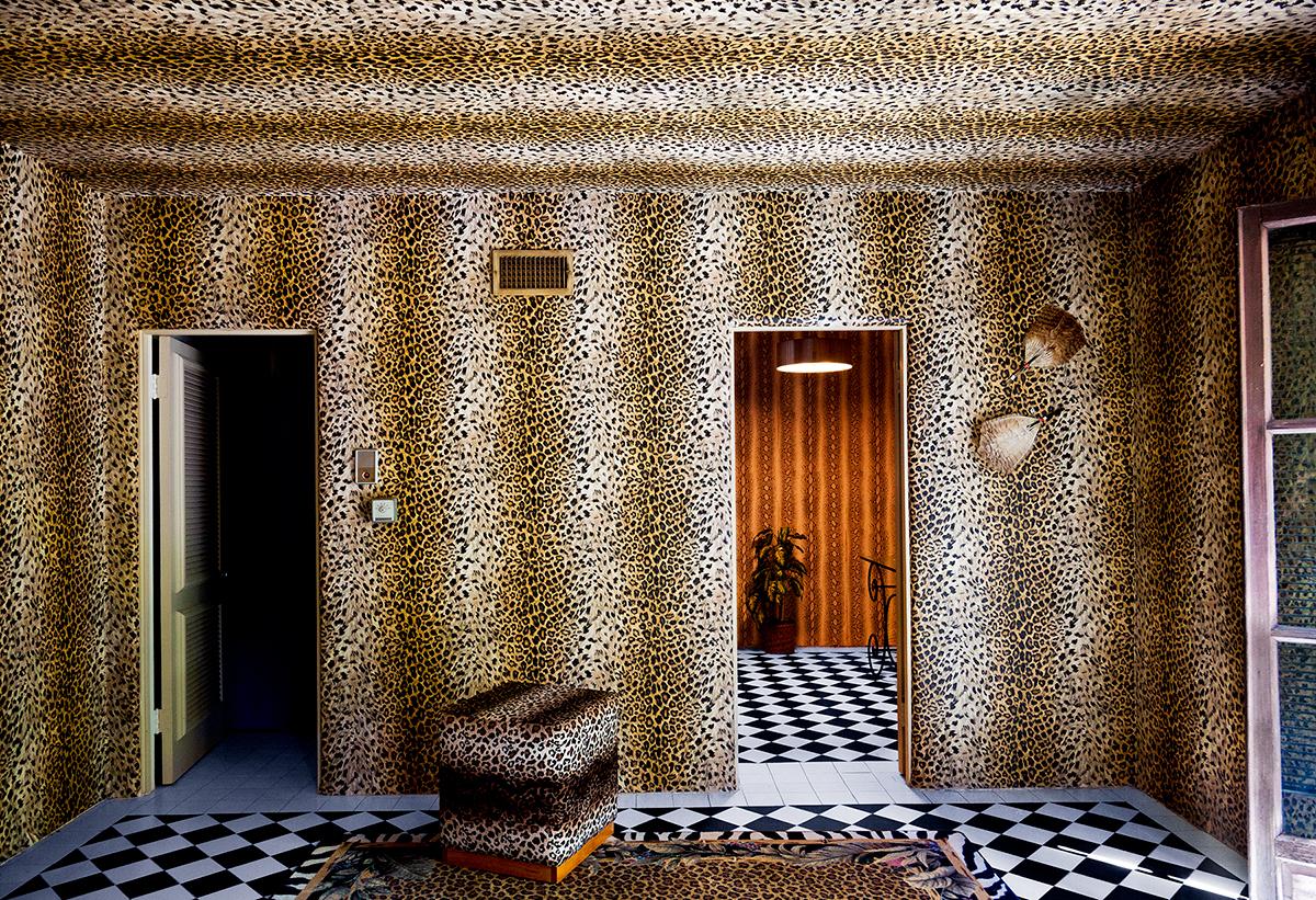"Lee's Gone" is a 24 x 36 inch archival pigment print by photographer Nancy Baron. This photograph features a room with the ceiling and walls covered in cheetah/leopard patterned wallpaper. This photograph is an edition of 5. Additional sizes are