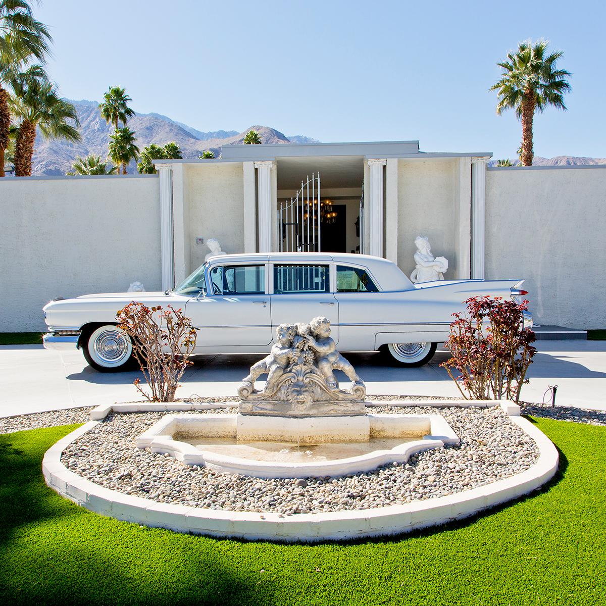 Piazza de Liberace by Nancy Baron is an 16.5 x 16.5 inch archival pigment print, available in an edition of 10. The photograph features the front of Liberace's house, with a white car and small fountain in front. 
This photograph is from Nancy