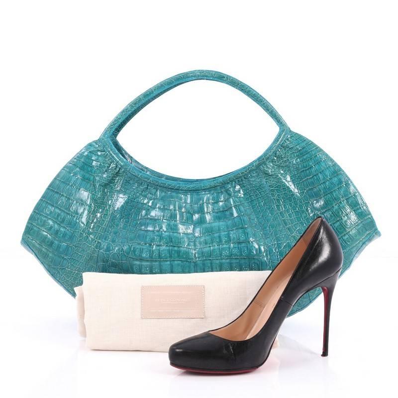 This authentic Nancy Gonzalez Crescent Shoulder Bag Crocodile Large is a luxurious, angular bag showcases a feminine silhouette. Crafted in genuine teal crocodile skin, this sleek bag features dual looped top handles, crescent shape and gold-tone