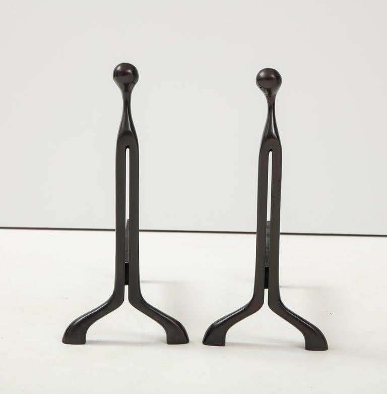Pair of custom finished aged bronze andirons by Nancy Rubens. Andirons have a sleek modern silhouette which can be utilized in most decor.