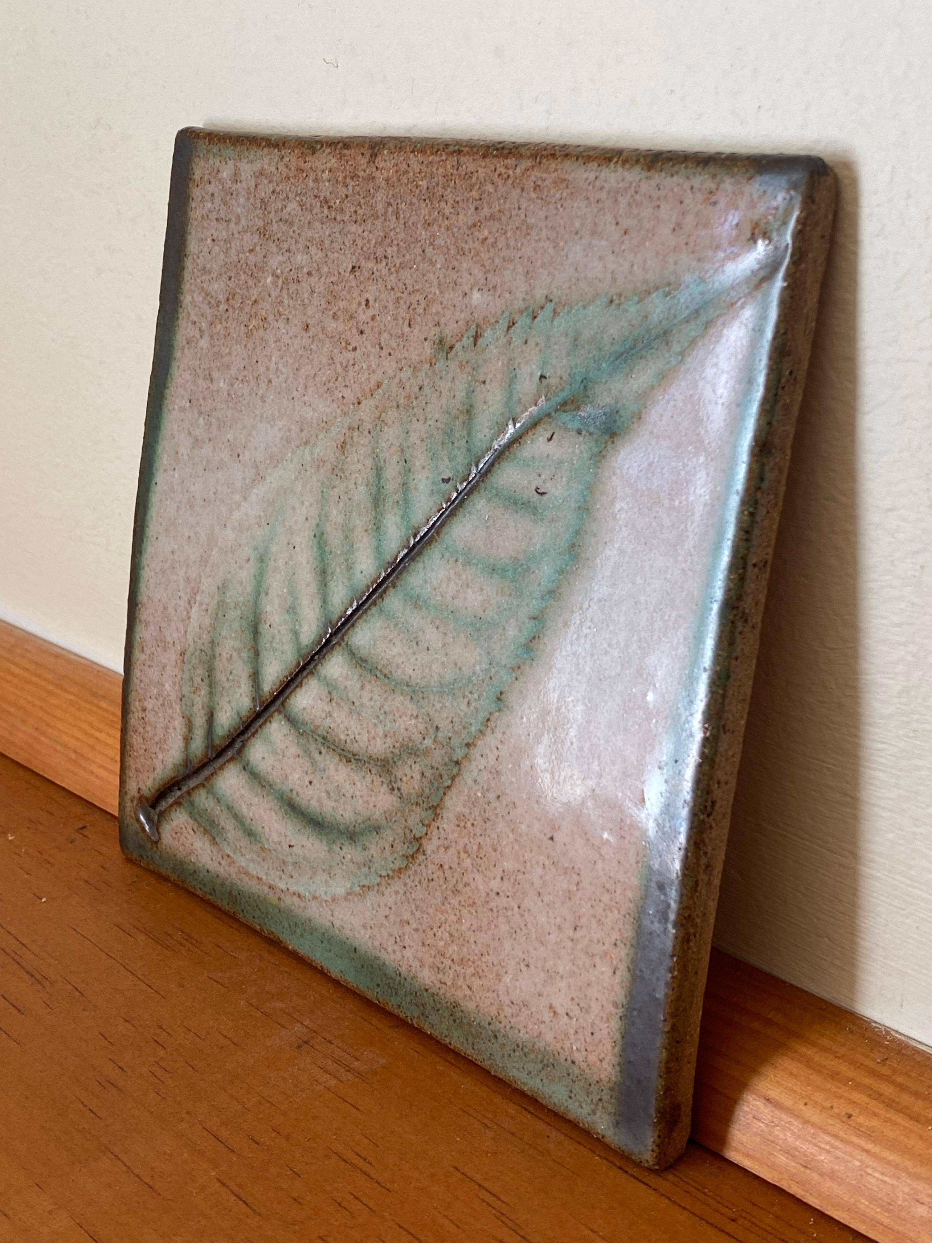An early 1980s stoneware tile by Nancy Wickham Boyd featuring a green leaf motif. The sgrafitto design is highlighted with green, brown and grqphite-colored glazing. Like quite a few well-known NYC potters Nancy got her start working for a few years