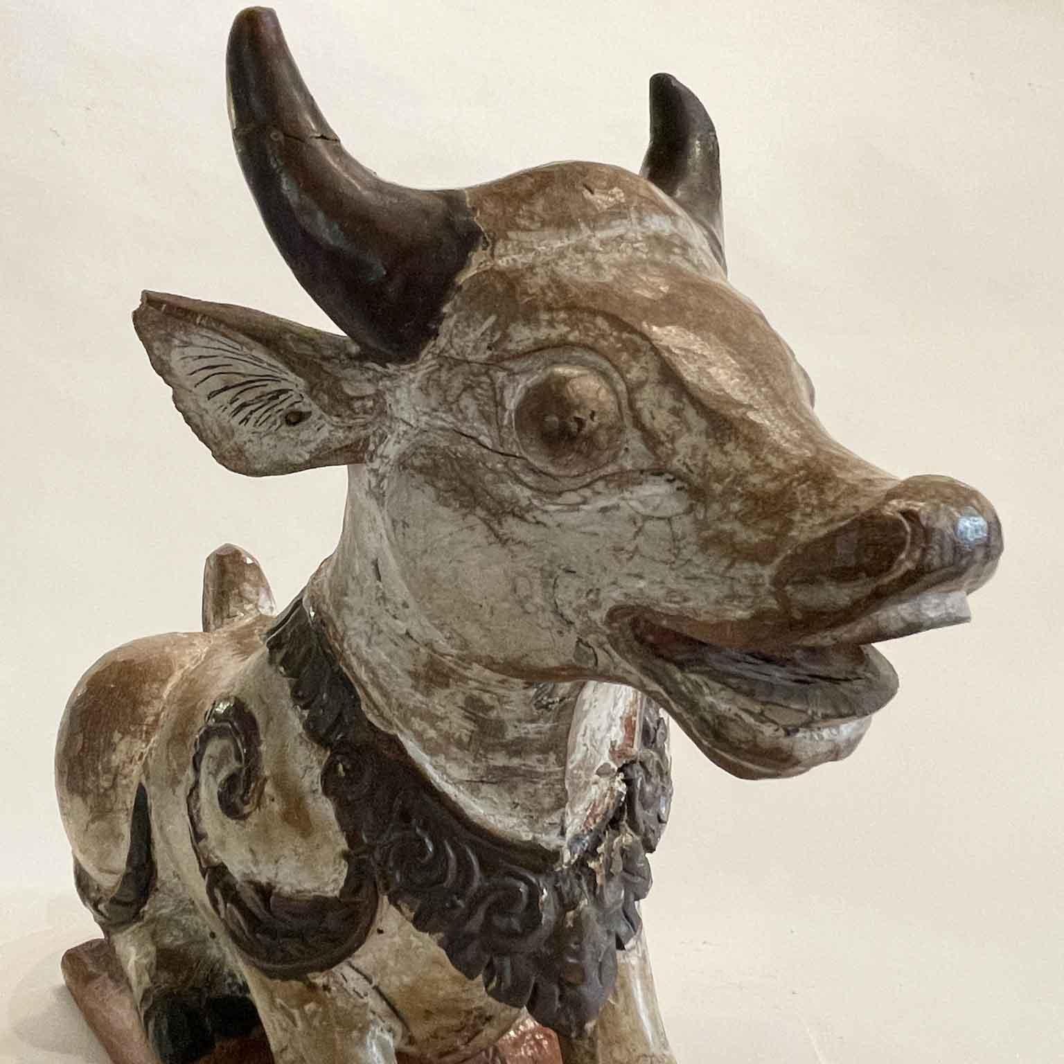 Vache Nandi en bois sculpté et laqué  visiblement antique et sculpté à la main, en provenance de l'Inde. Cette sculpture en bois présente une magnifique patine due à l'âge et a été peinte à la main avec un mélange de couleurs blanches vives. Selon