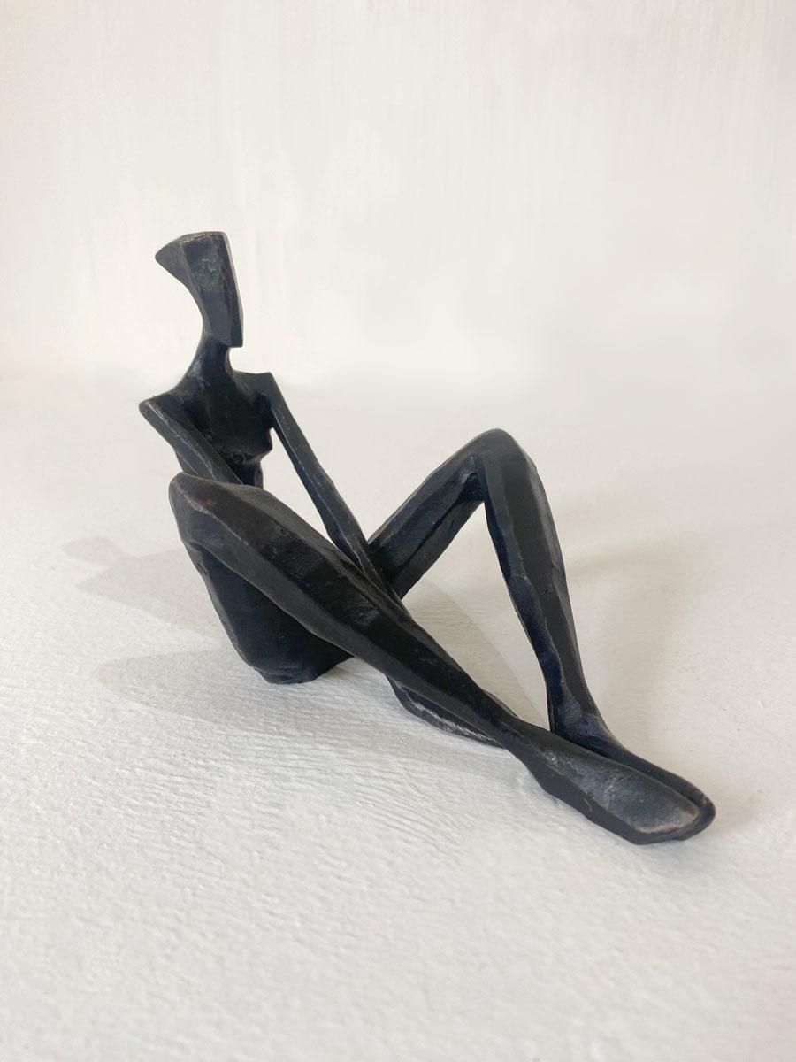 Nando Kallweit's Giselle II captures a minimalist, abstract female figure seated in a casual, cross-legged pose. 

The bronze sculpture exhibits a sleek, matte finish that enhances its modern appeal. The woman's elongated limbs and simplified form