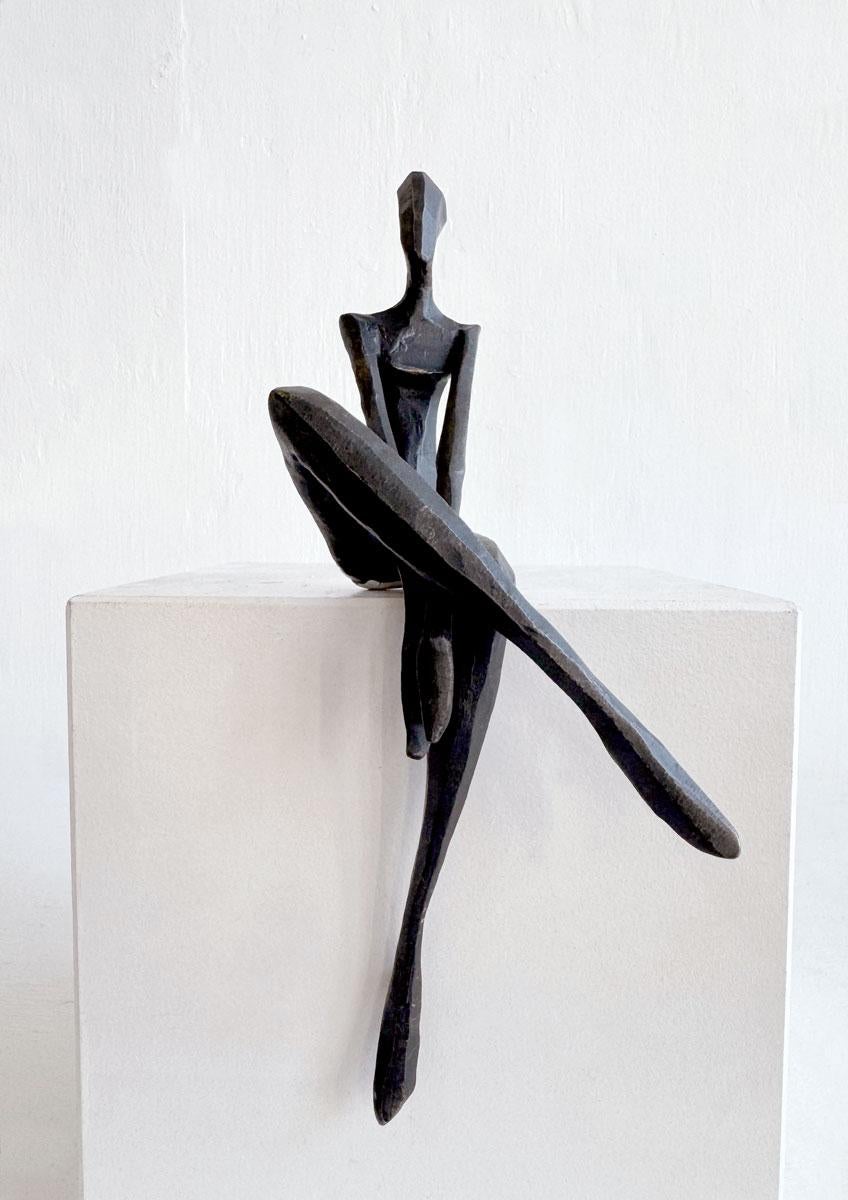 Nando Kallweit
s Silvi captures a minimalist, abstract female figure seated in a casual, cross-legged pose. 

The bronze sculpture exhibits a sleek, matte finish that enhances its modern appeal. The woman
s elongated limbs and simplified form