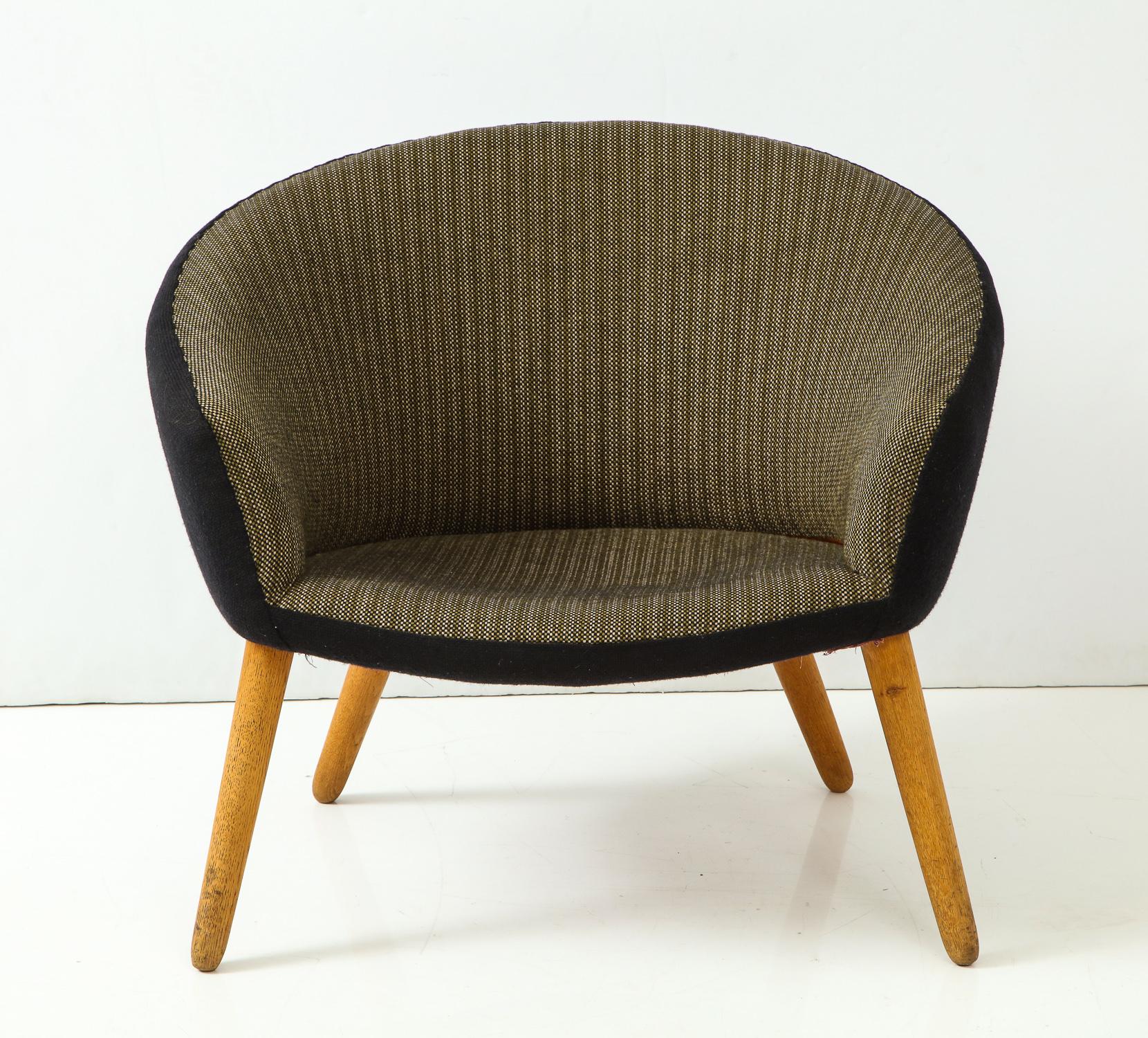 Curved-back lounge chair with splayed oak legs and original two-tone fabric. Designed by Nanna Ditzel and produced in Denmark by A.P. Stolen, circa 1950s. A nice vintage example; the two-tone fabric accentuates the curvilinear shape of the back.