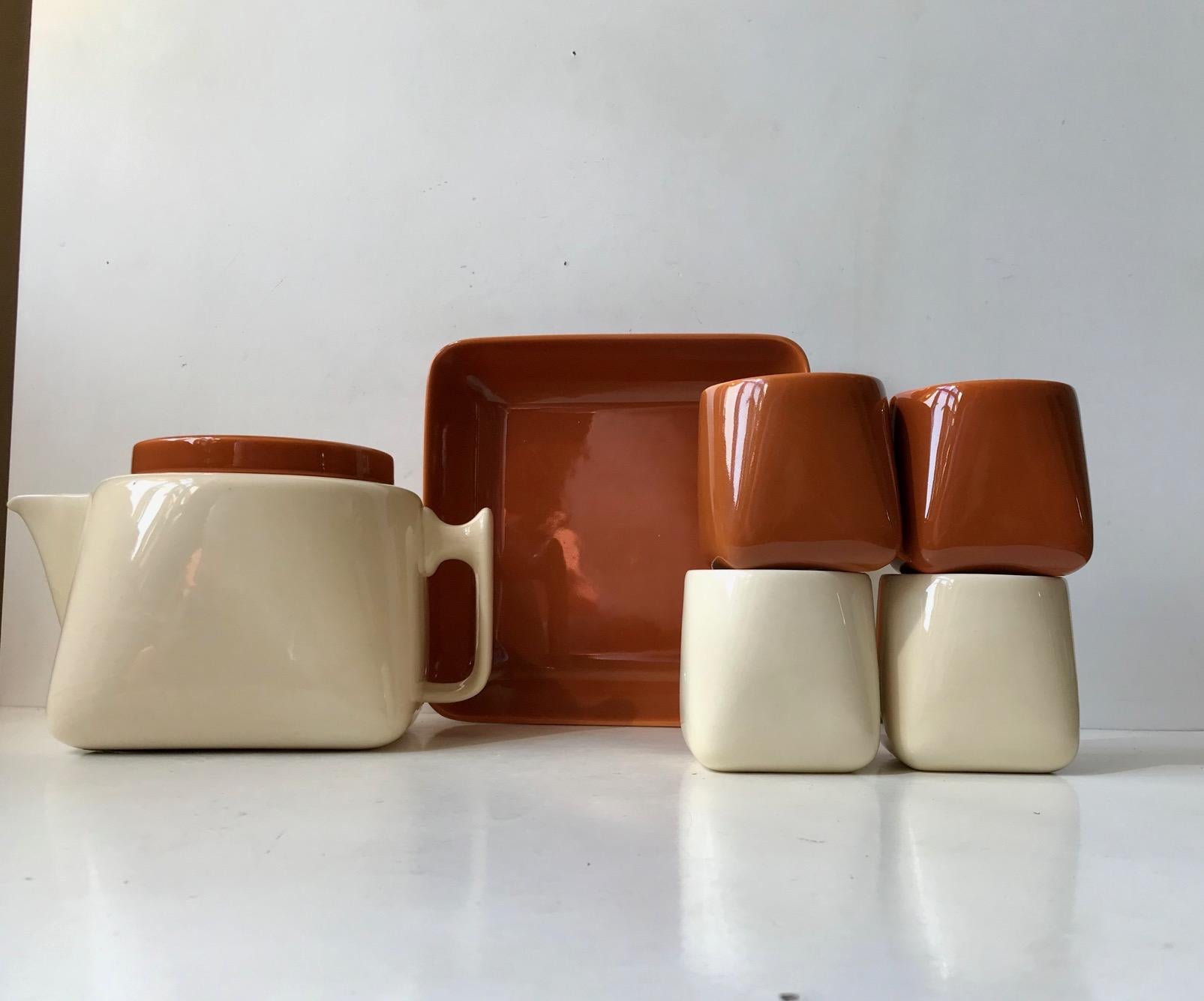 A rare tea service consisting of a teapot, cookie bowl and 4 cups. The shape starts of as a square at the bottom and transform fluently into a circle at the top. All pieces features monochrome glazes in burnt/caramel orange and creme pastel. This