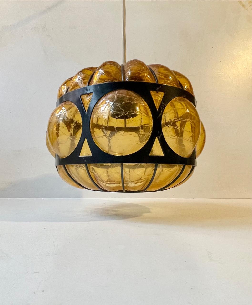 A caged hand blown amber glass pendant light. The glass displays texture and the steel 'cage' is powder coated black. Manufactured by RAAK in Holland and designed by Nanny Still circa 1960-70. Measurements: 23x20 cm.