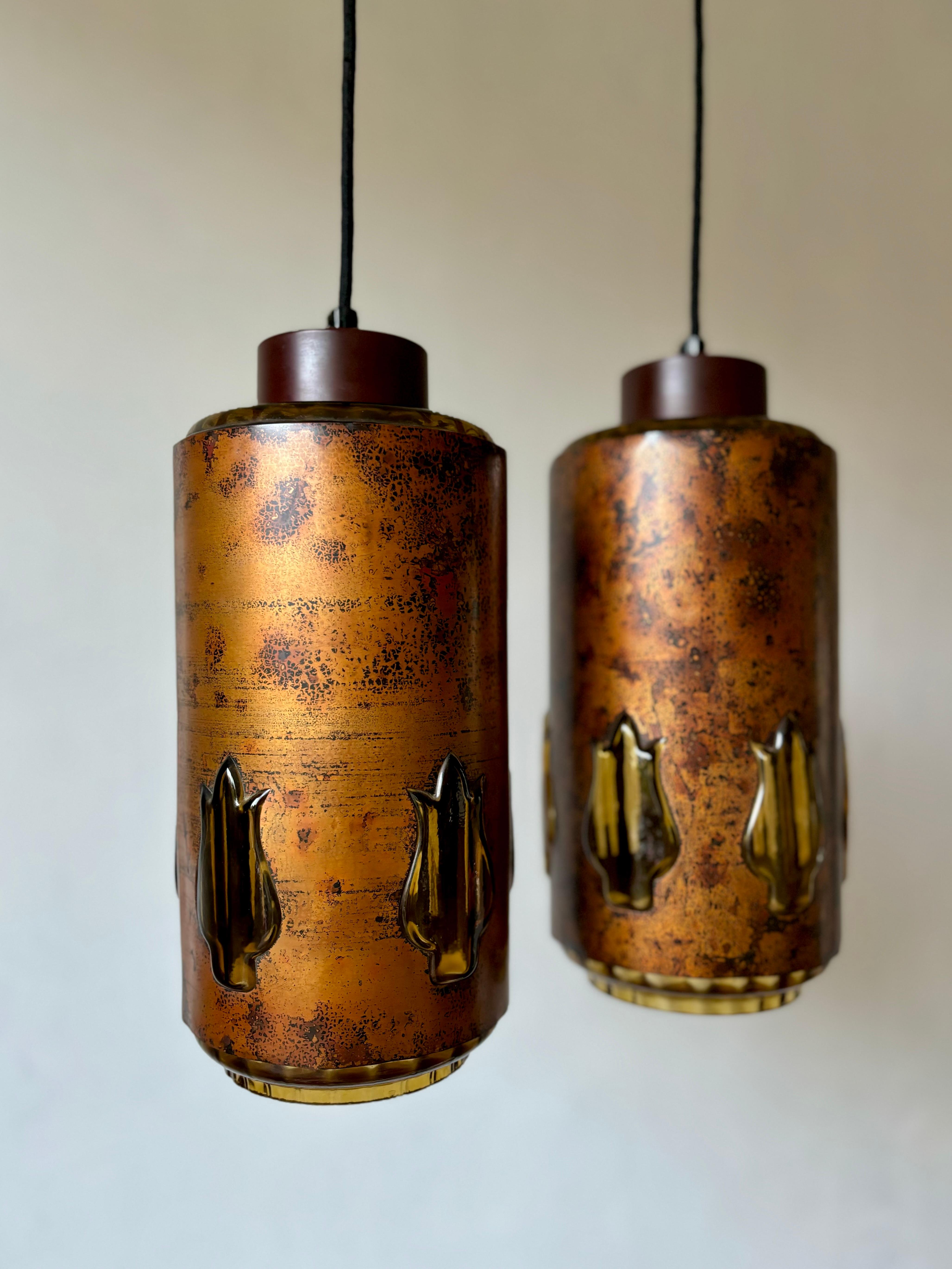 Patinated oxidized copper midcentury brutalist pendants hand-crafted by Nanny Still McKinney for RAAK - each unique in their execution. Cylinder shaped body with thick amber colored glass on the inside, bottom and top and five thick amber colored