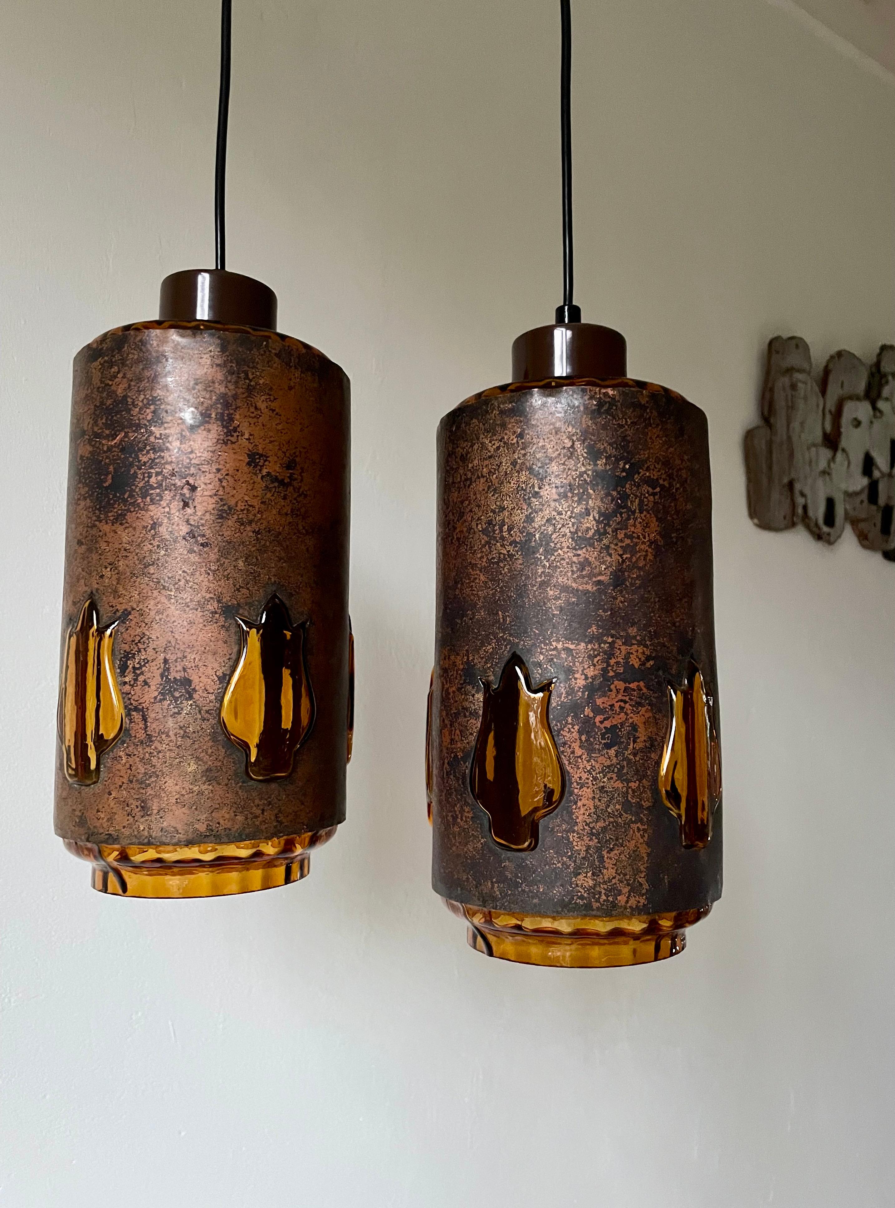 Patinated oxidized copper midcentury brutalist pendants by Nanny Still McKinney for RAAK - each unique in their execution. Cylinder shaped body with thick amber colored glass in the inside and five thick amber colored glass decorations protuding