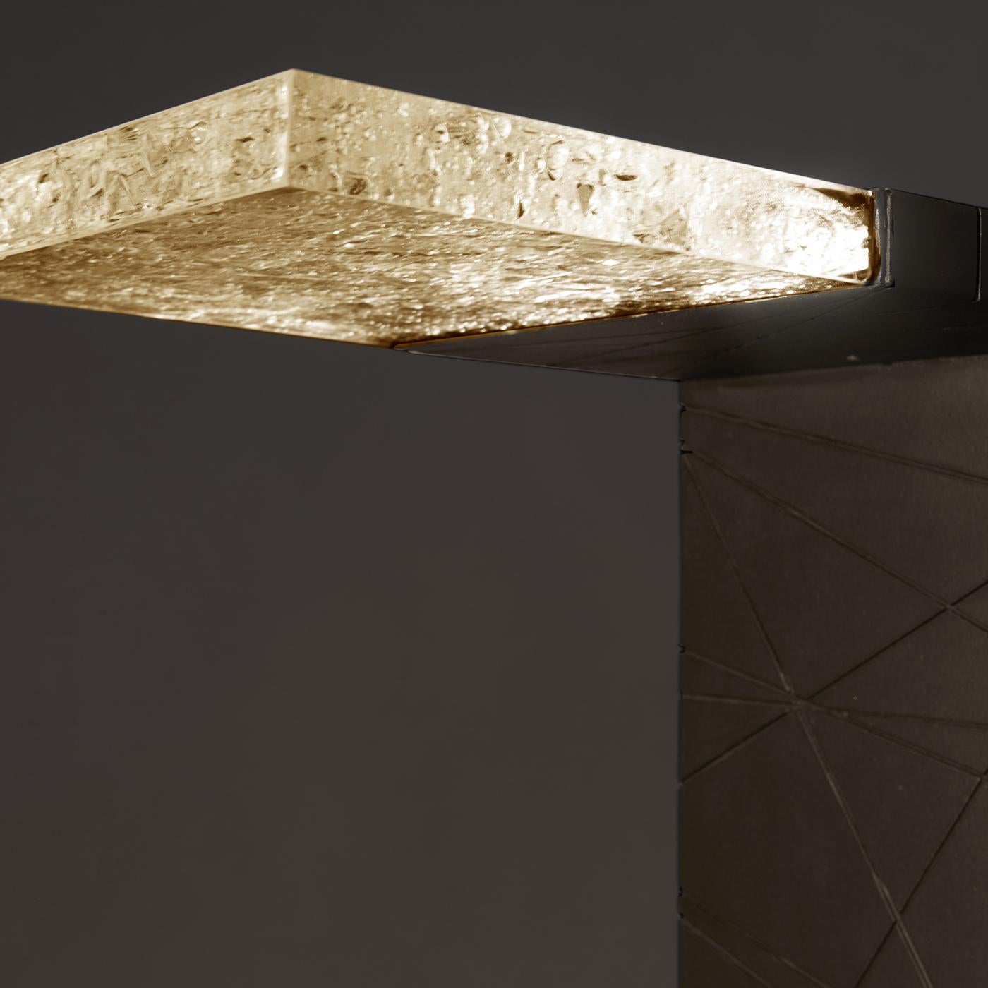Defined by a sleek, essential silhouette of majestic proportions, this floor lamp blends form and function. Handcrafted of ground volcanic rock with a rust finish, the L-shaped body features at the end of the top arm a clear element containing