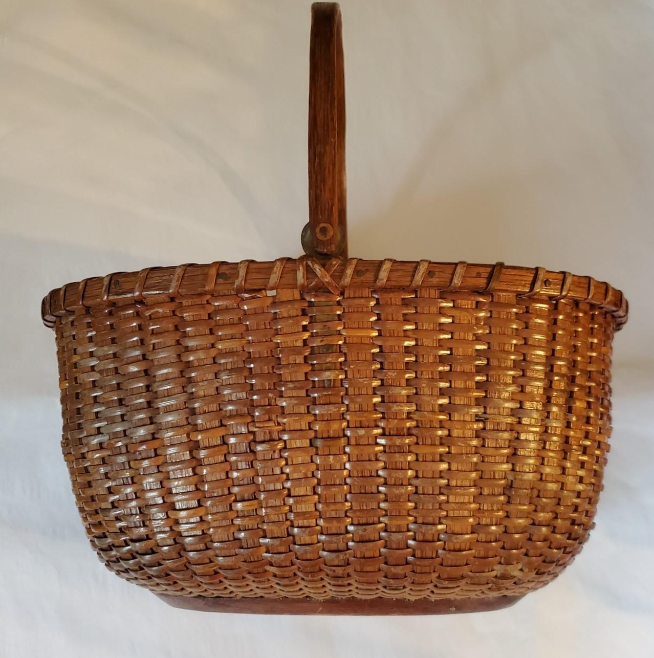 Antique Nantucket Basket by A.D. Williams (Nantucket: 1867 - 1927), circa 1890, an oval open Nantucket basket with cane weave on oak staves, with his distinctive carved swing handle attached to round brass ear extending beyond end of handle and