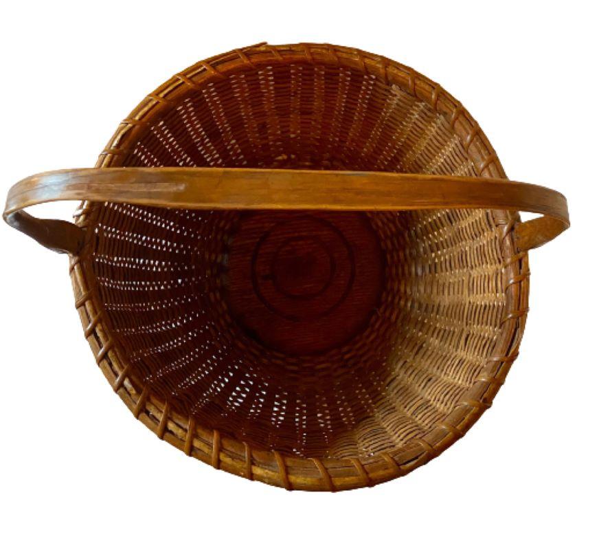 Vintage Nantucket Basket, by Mitchy Ray (1877 - 1956), circa 1920s, a large open round basket with heavy wooden staves, cane weave, solid oak bottom plate with two inscribed rings, and a carved swing handle attached to fairly long metal ears. The