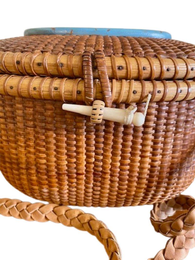 Vintage Nantucket Purse by Barbara Grey, circa 1995, un panier Nantucket ovale couvert, avec un tissage en canne sur des douves en rotin, une bandoulière en cuir tressé, une cheville en os tourné, et ayant une belle scène de chasse à la baleine