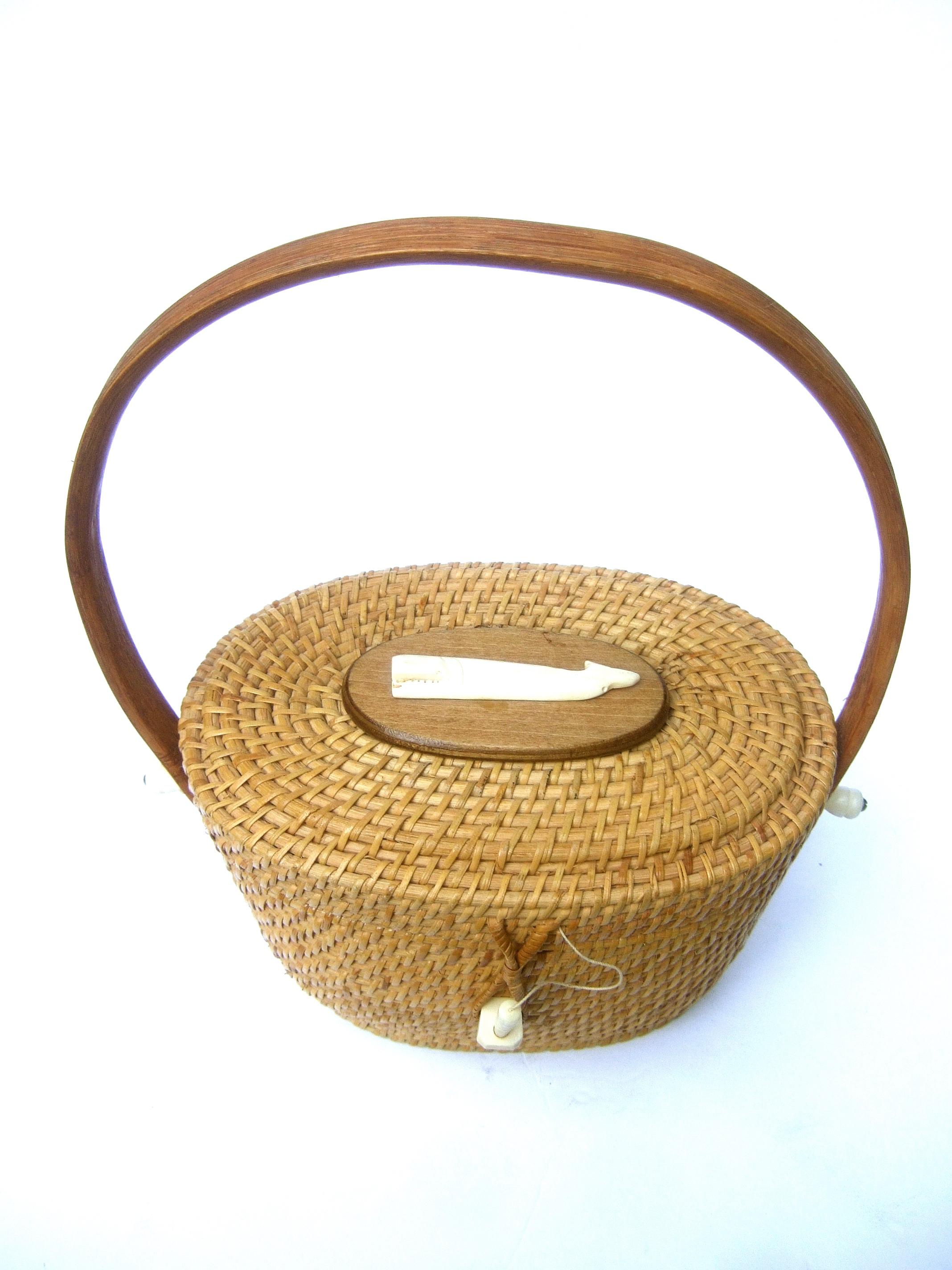 Nantucket style woven wicker resin whale handbag c 1980s
The iconic oval shaped basket handbag is adorned
with a carved resin whale figure mounted on an oval
wood plaque

Carried with a bentwood swivel handle. The clasp 
secures with a matching faux