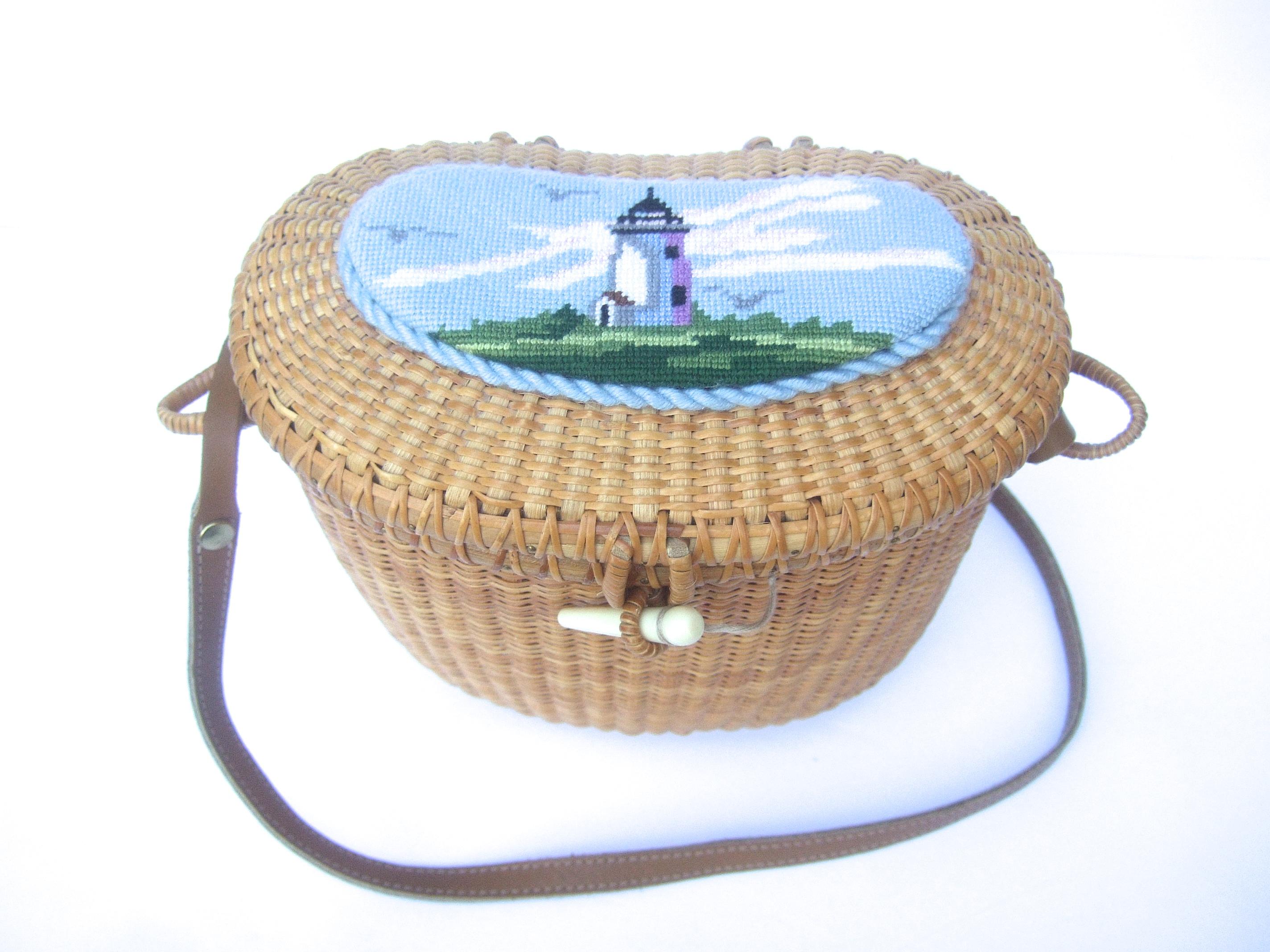 Nantucket style woven wicker rattan shoulder bag with needlepoint lid cover c 1980s
The charming light-weight woven wicker basket style shoulder bag is designed with a needlepoint lighthouse scene on the lid cover

Secures closed with a faux resin