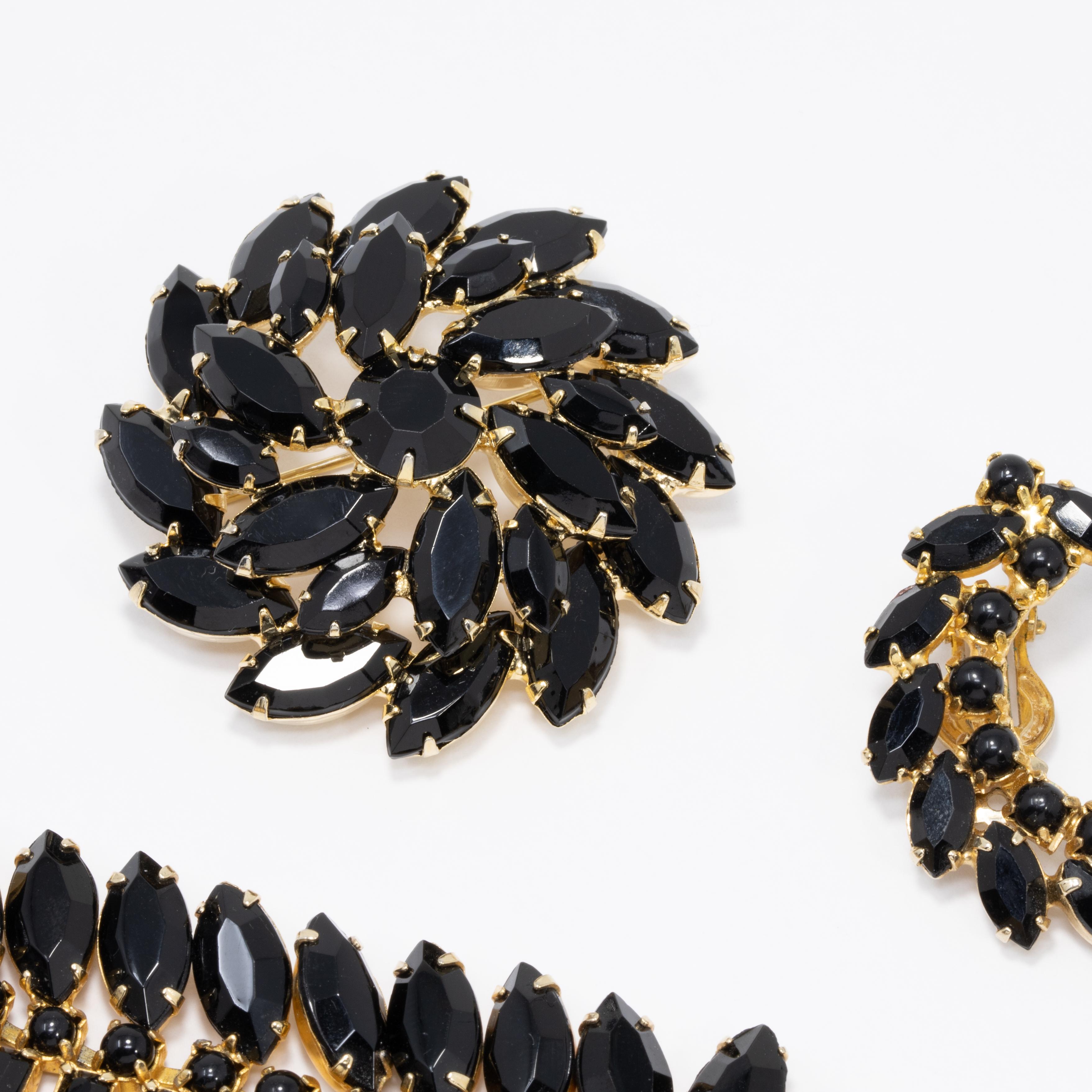 A stylish demi parure, featuring jet-crystal encrusted bracelet, pin brooch, and clip on earrings in gold tone. 

Brooch marked 