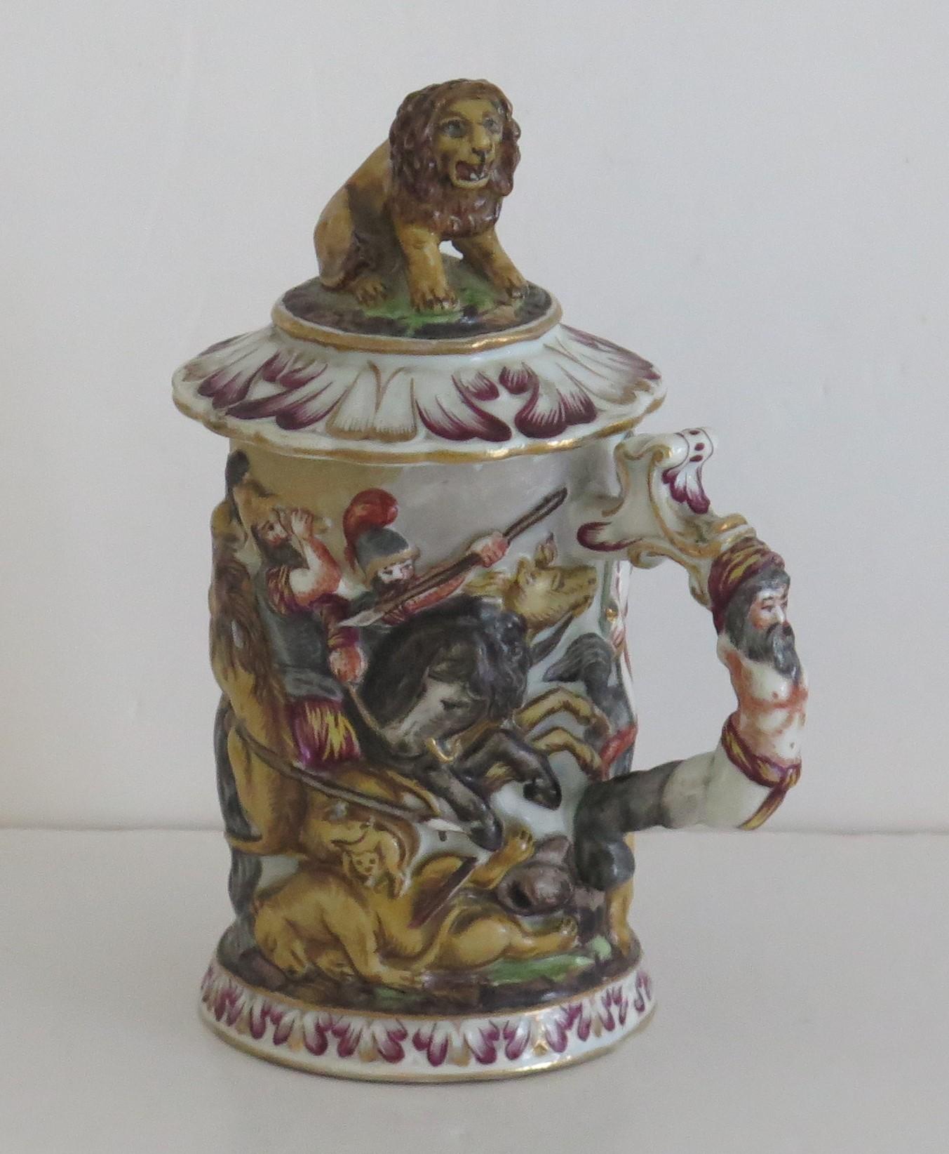 This is a Naples (Capodimonte) Porcelain Lidded Tankard with deep relief body, which we date to the early 19th Century and made in Naples, Italy.

The tankard is hand made with deep relief decoration of a hunting scene with men on horseback