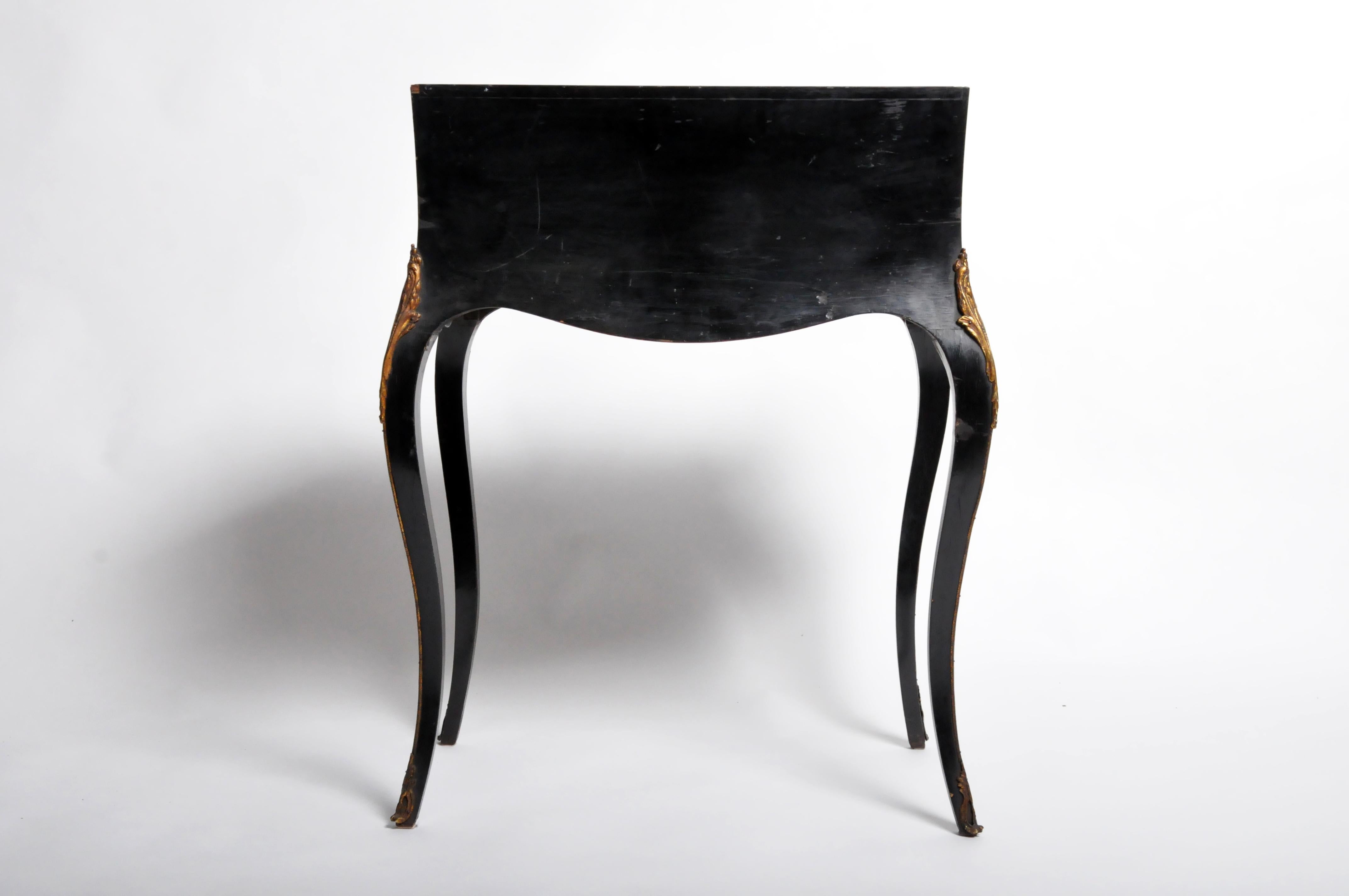 This petit fold-out bureau has many of the best-loved elements of “Second Empire” design – black lacquer, cast, and inlaid brass, and somewhat sensual curves. The piece is made from hardwood, veneered and lacquered black. Interior drawers are