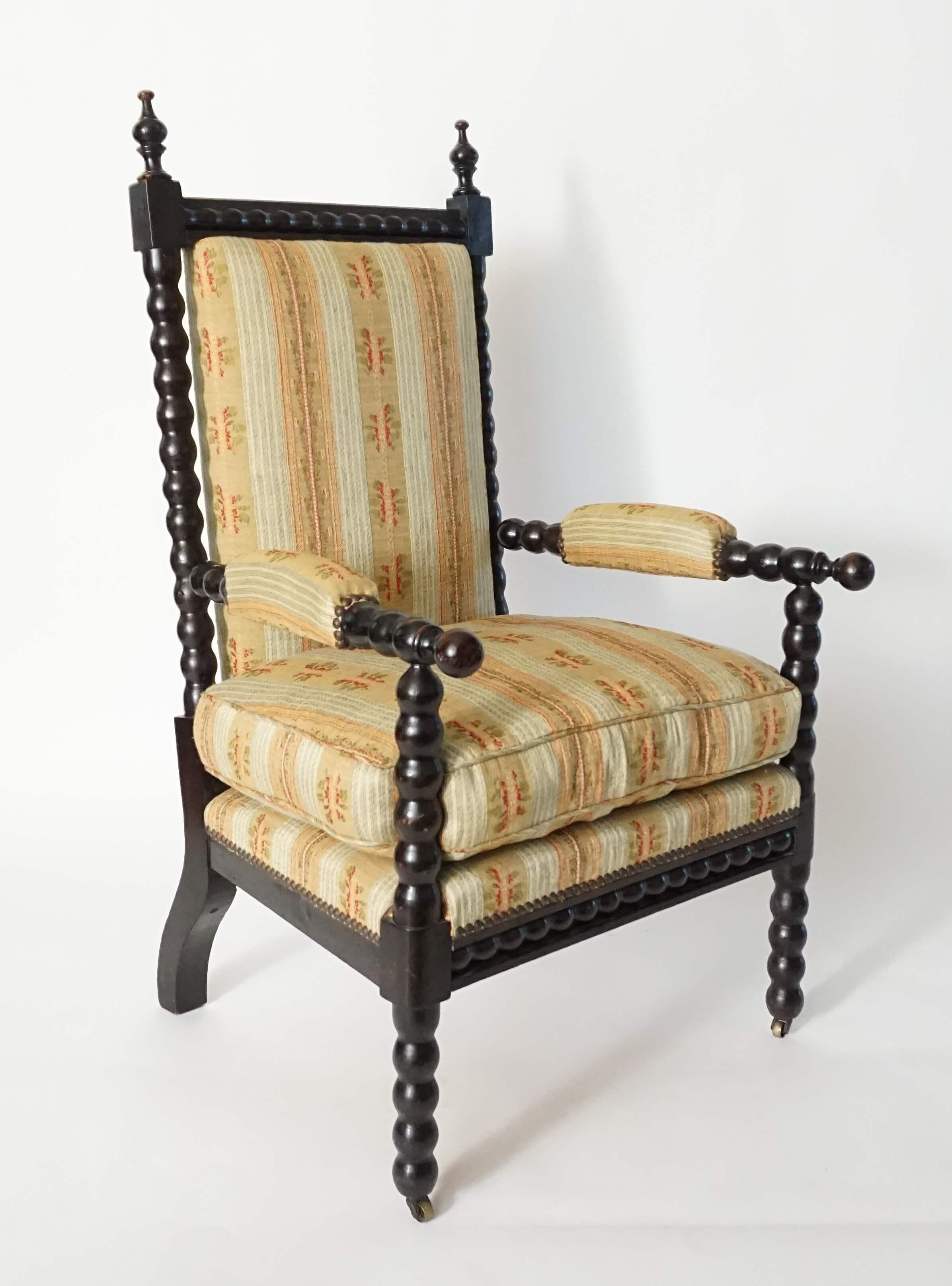 Elegant circa 1860 French Napoleon III period armchair having original ebonized finish on spool or bobbin-turned chestnut frame, the rectangular upholstered back with inset-bobbin-channel top rail connecting finial-topped stiles joining upholstered