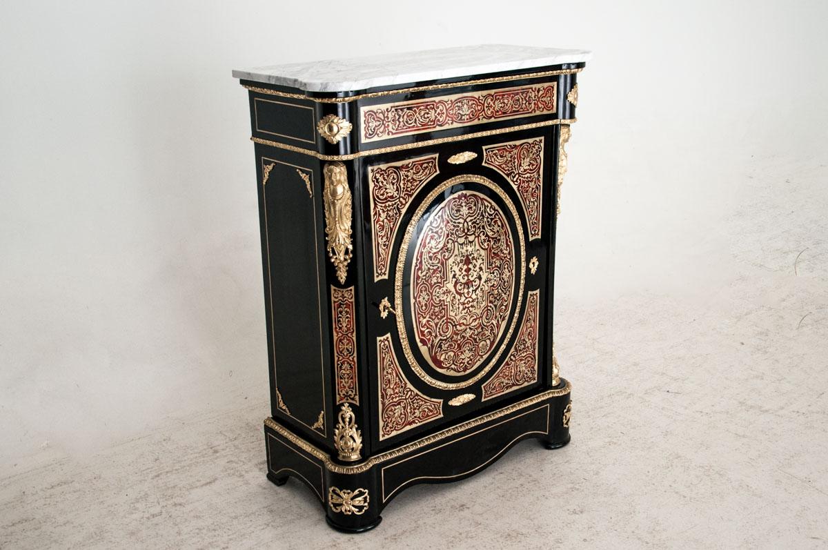 Cabinet fabriqué au 19e siècle, en France, sur le modèle du mobilier baroque du 17e siècle de l'ébéniste français A. Ch. Boulle.
Ce meuble est une armoire à une porte avec une étagère à l'intérieur.
Cette commode est ornée à l'avant d'une