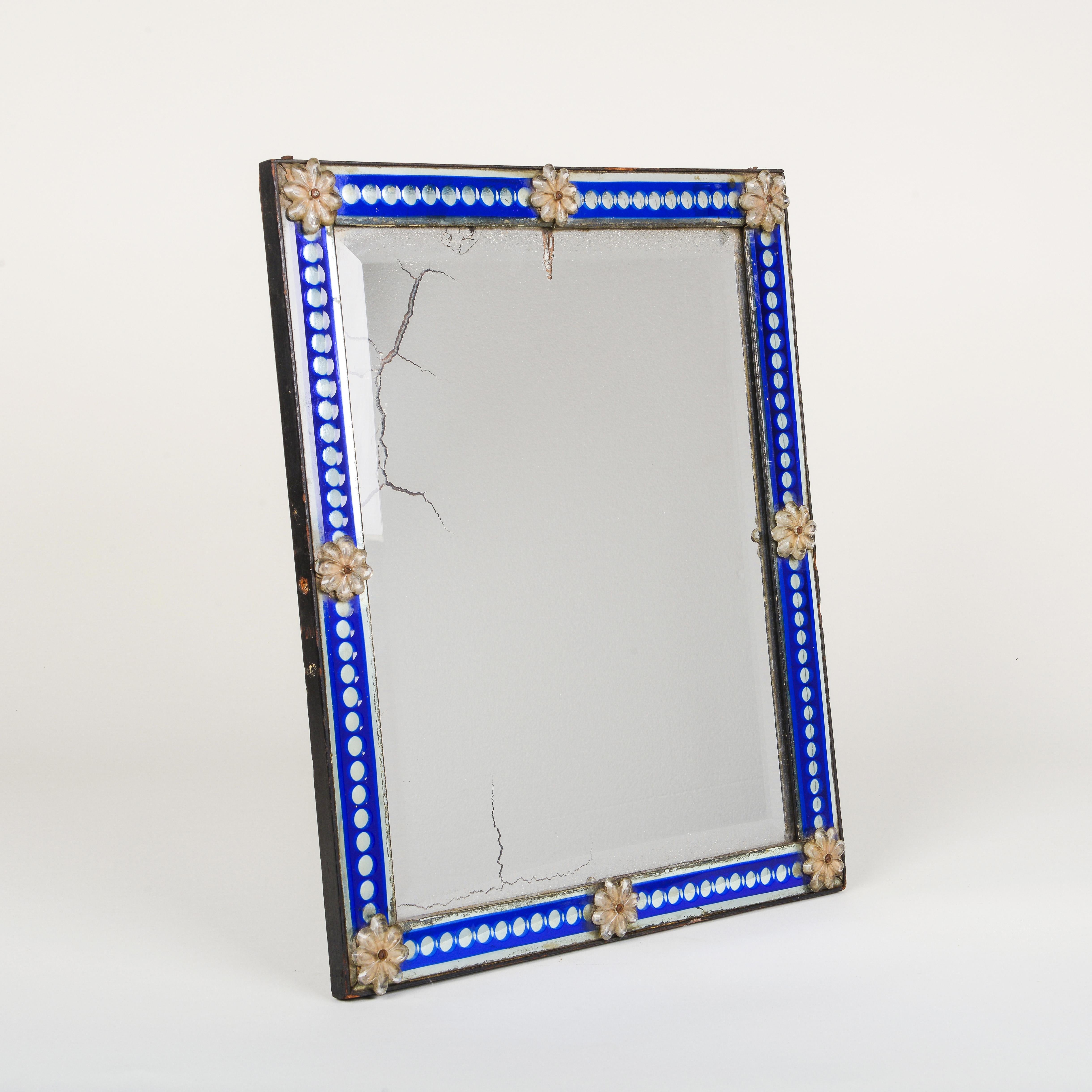 The rectangular beveled mirror plate bordered by clear dots on a blue ground surround, mounted with daisy form glass appliques. With easel form back.