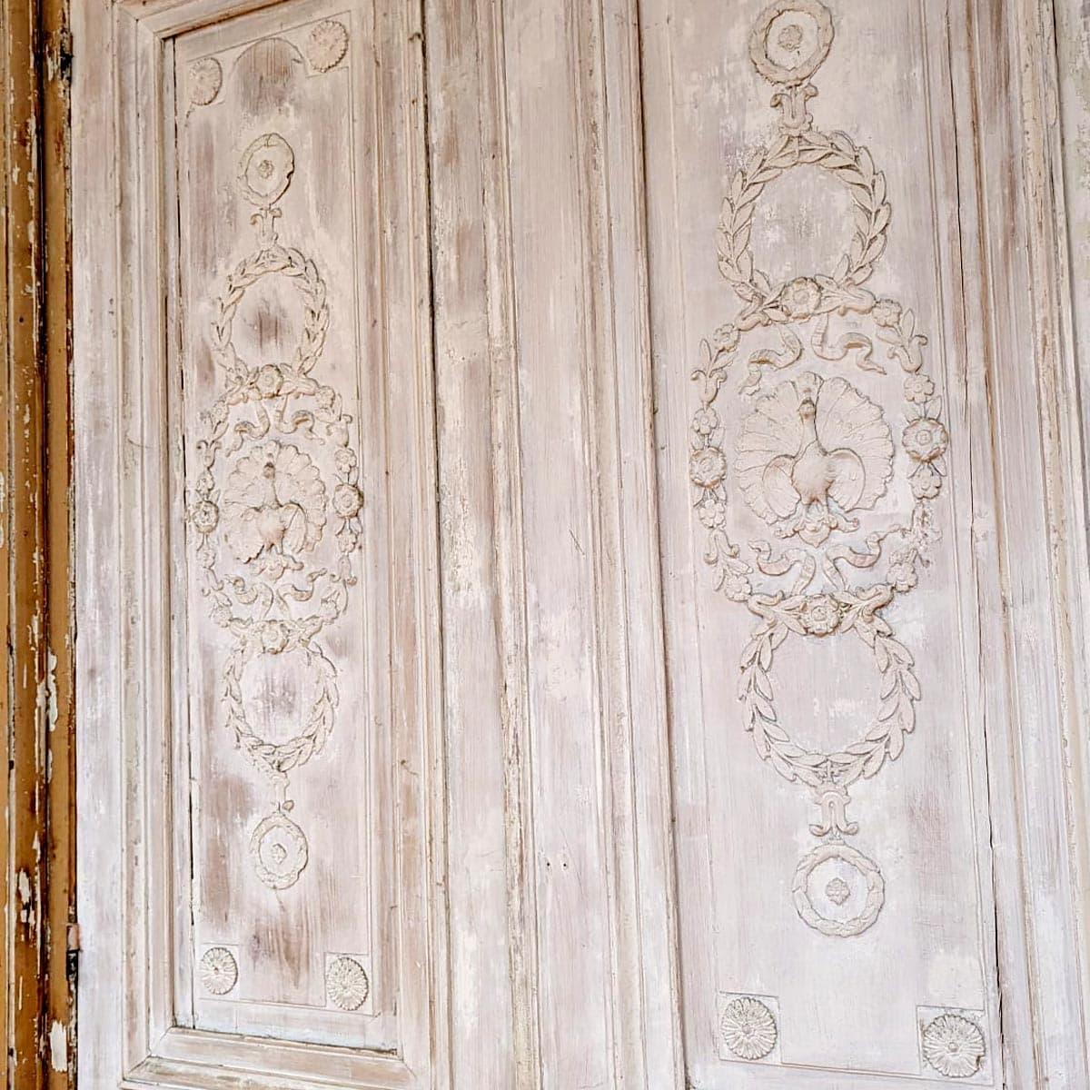 Magnificent double door in carved wood from the Napoleon III period, featuring highly detailed ornamentation with central peacock motifs surrounded by floral garlands and classical medallions. The original paint has been naturally patinated over
