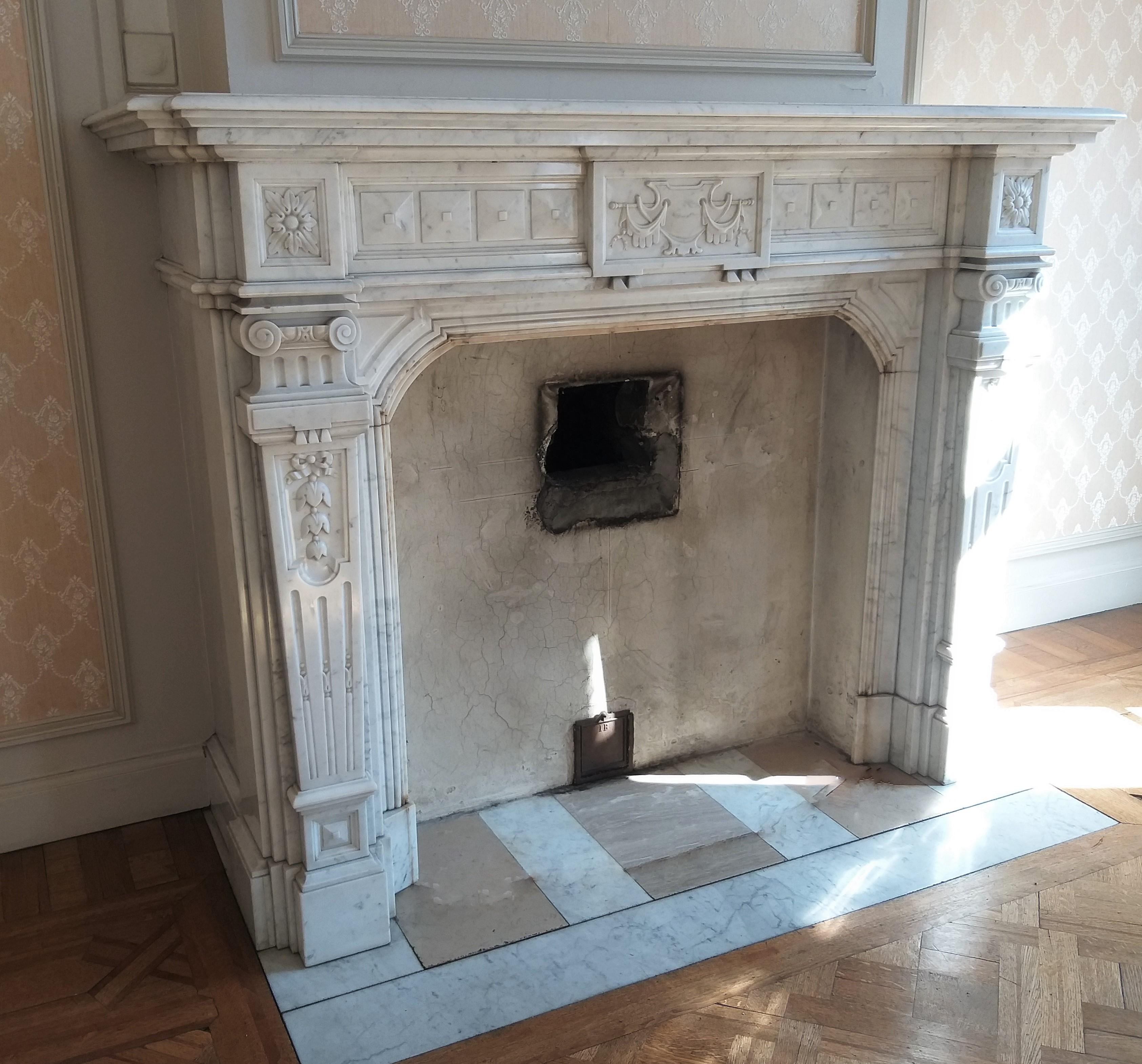 This Napoléon III fireplace made out of Carrara marble dates from the late 19th century and is rich decorated.
The moulded shelf rests above a panelled frieze with in the center a tablet, depicting a sheld and drapery. (a dentil-detail, under-left,