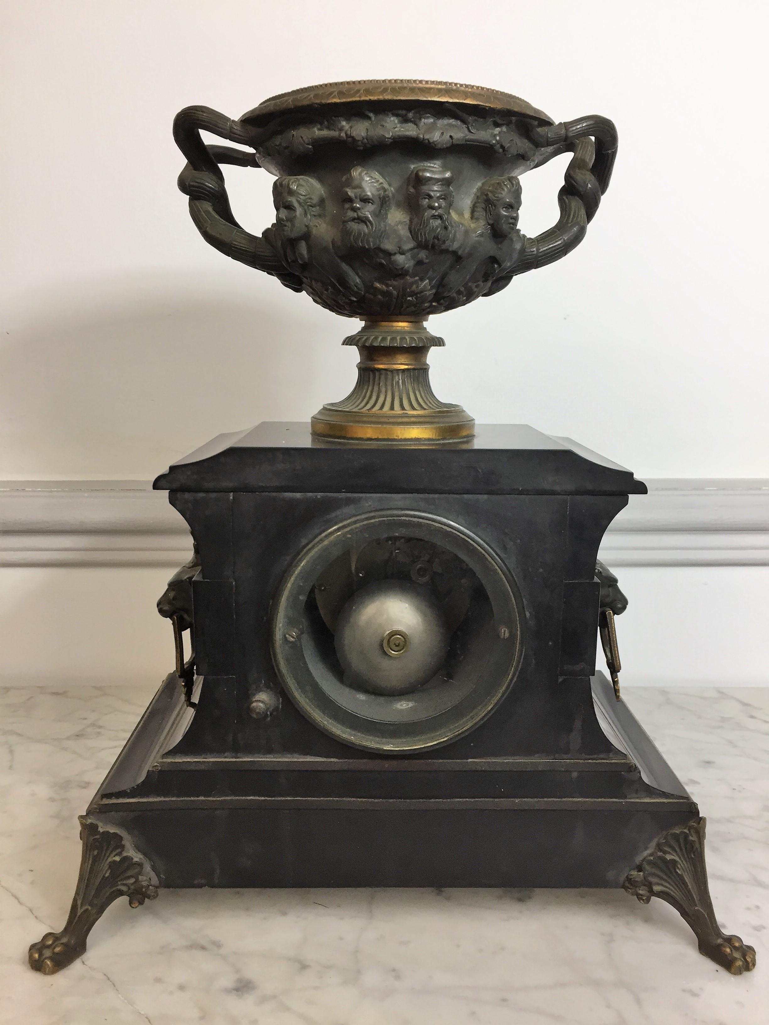 Beautiful antique fireplace set consisting of a clock and a pair of cassolettes. The black marble clock rests on lions' feet and is surmounted by a bronze engraved Medici vase with eight faces of Greek gods and adorned with a garland of vine leaves