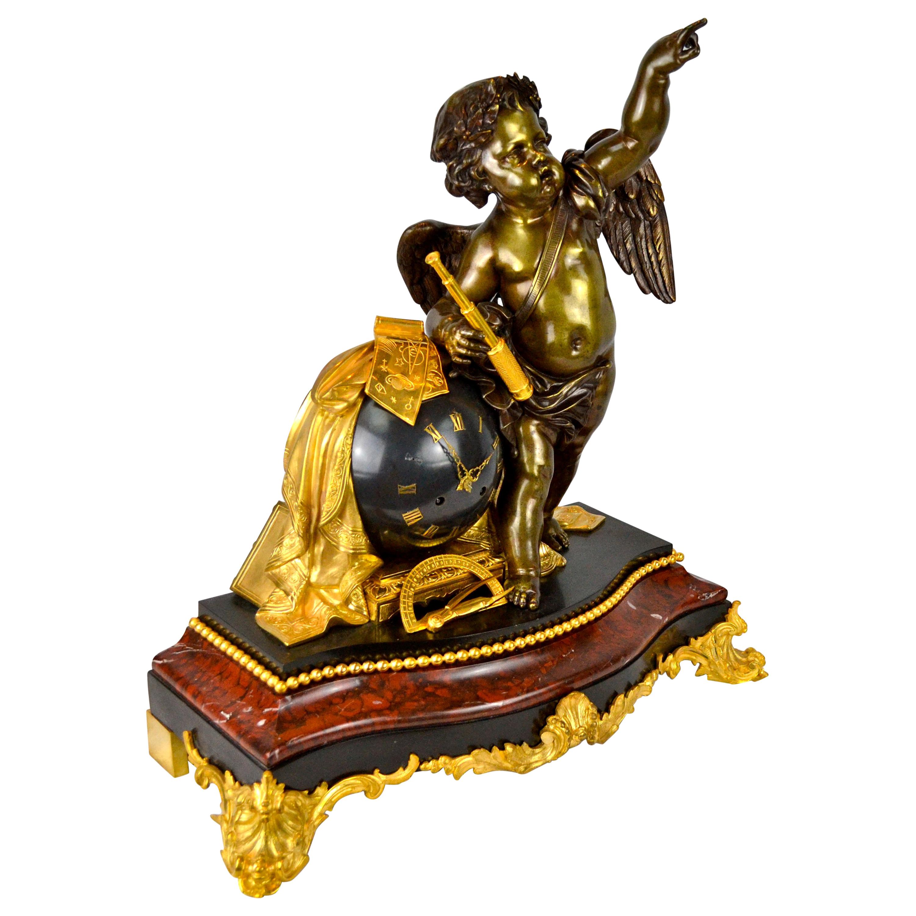 Napoleon III figural astronomical sciences clock. The patinated bronze winged putto stands beside the ‘blued’ bronze globe of the world housing the movement; he holds scientific instruments, telescope, calibers etc. in one hand and points to the