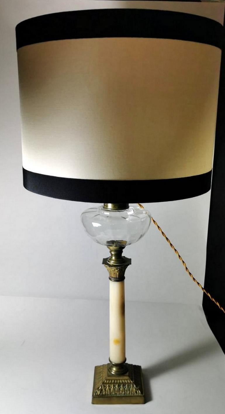 Empire style table lamp in the shape of a column; the body is in refined Afyon Miele marble from Carrara; the Corinthian capital and base are in gilded bronze casting that time have blackened; the container for oil is in a smooth crystal; in fact,