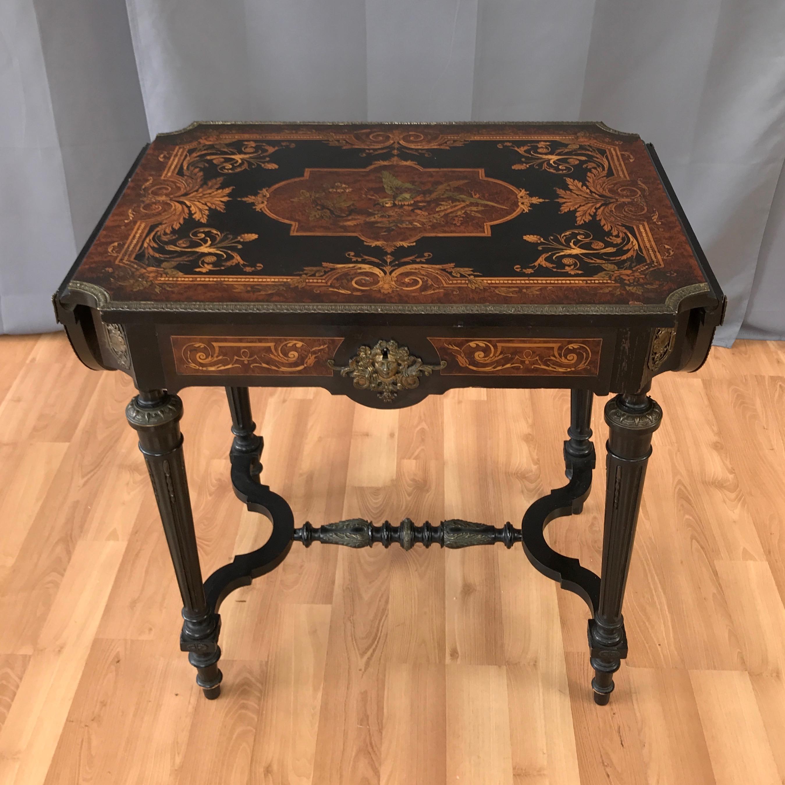 A mid-19th century Napoleon III drop-leaf salon or writing table with drawer, displaying wonderfully executed marquetry and ormolu decorations throughout.

Ebonized mahogany top, frame, and turned tapered legs, with a pair of leaves and single